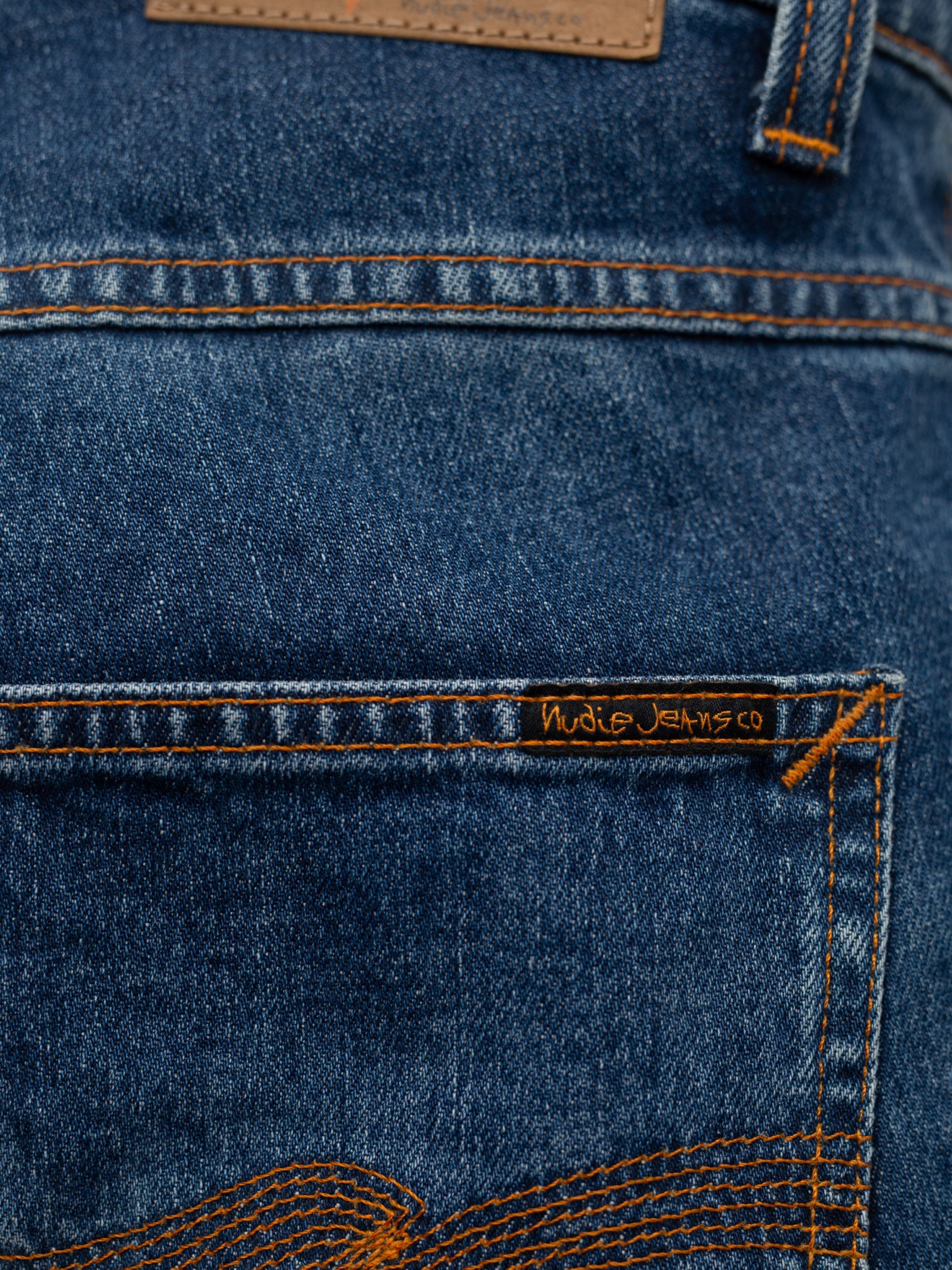 Nudie Jeans Grim Tim Life Tracks, close-up of the back pocket and orange threads on mid blue organic cotton stretch denim.