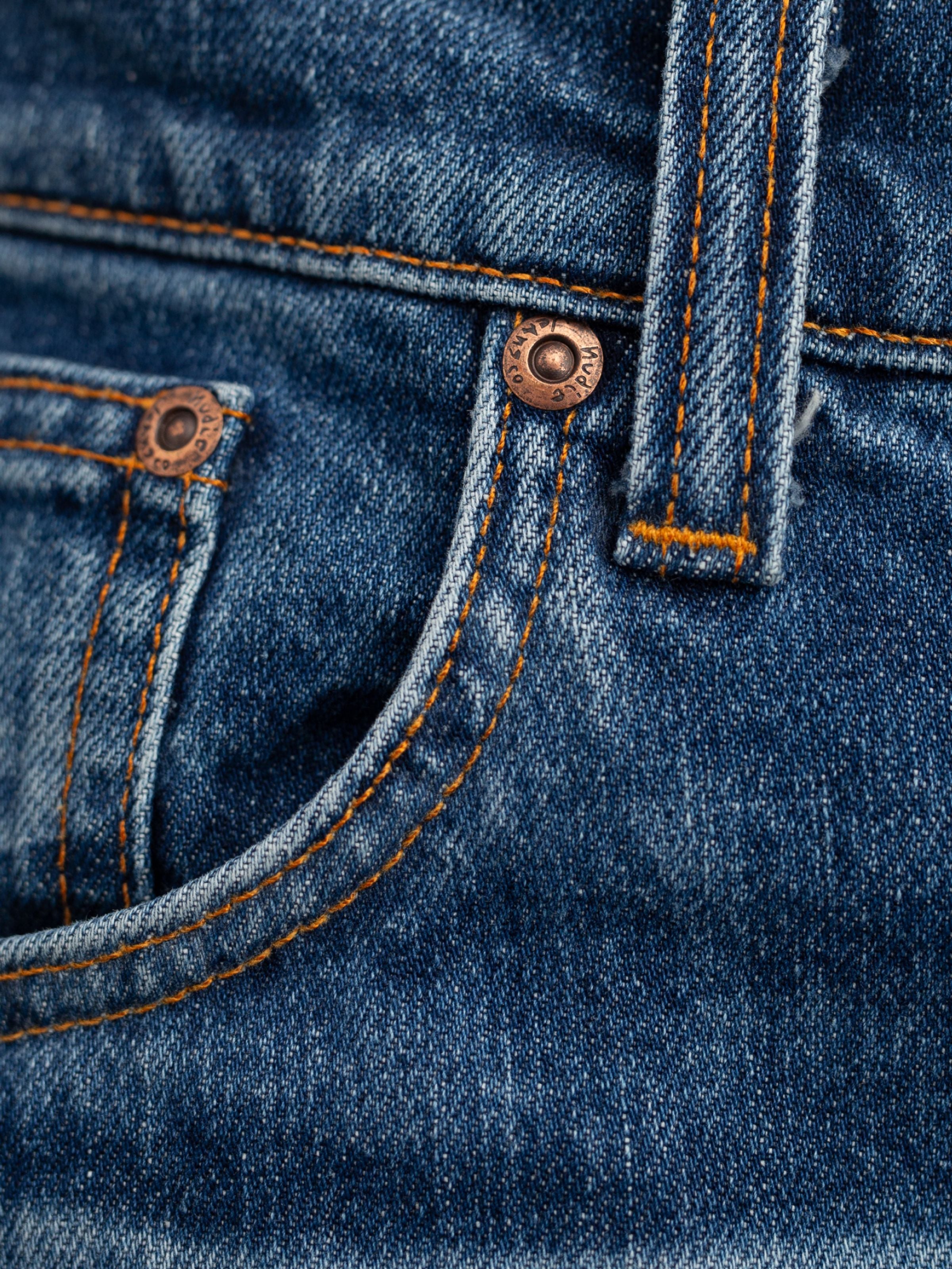Nudie Jeans Grim Tim Life Tracks, a close-up of the copper rivets and orange stitching on blue organic cotton stretch denim.