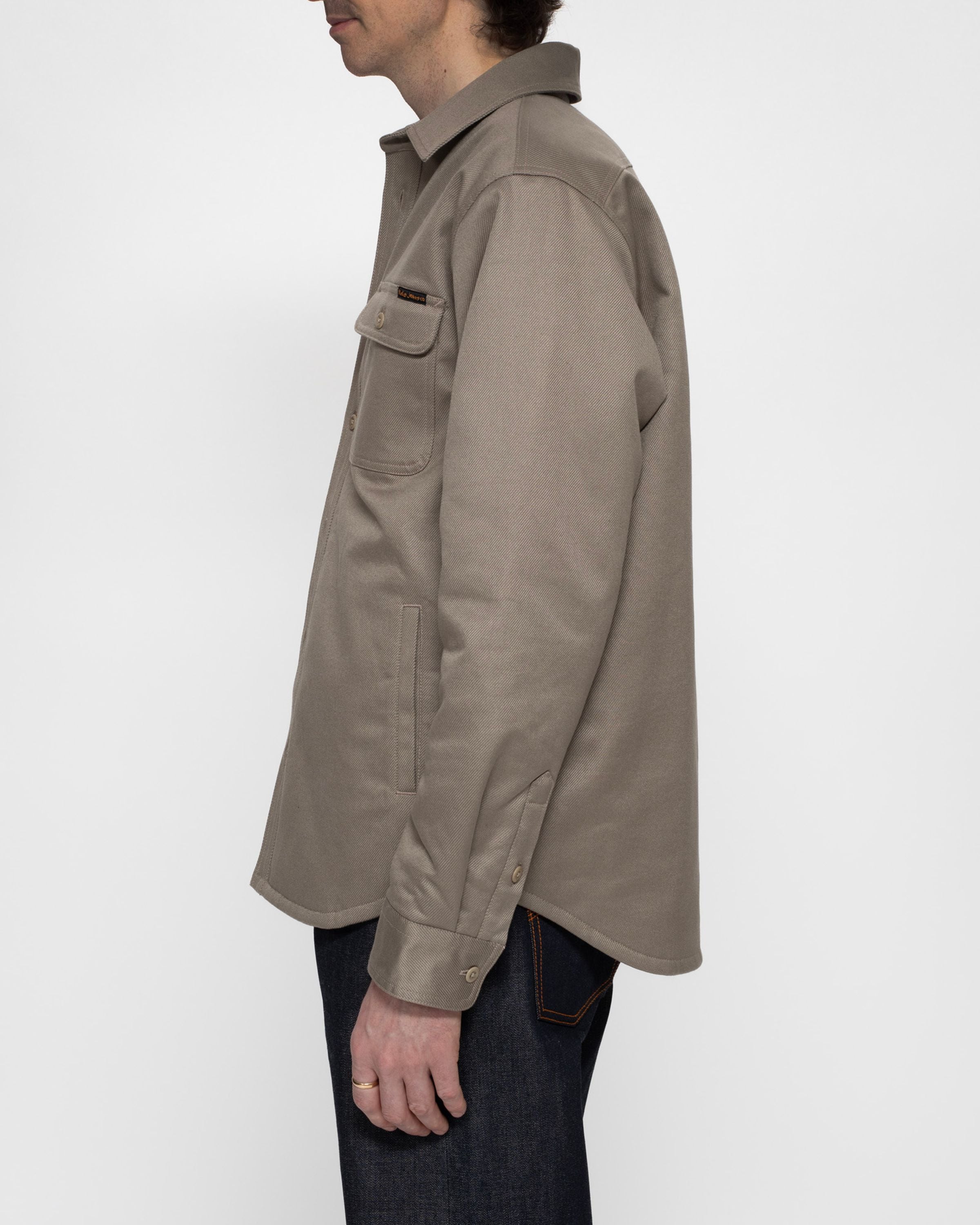 Nudie Jeans Glenn Padded Shirt in Mud, a regular fit organic cotton twill overshirt shown from a side profile.