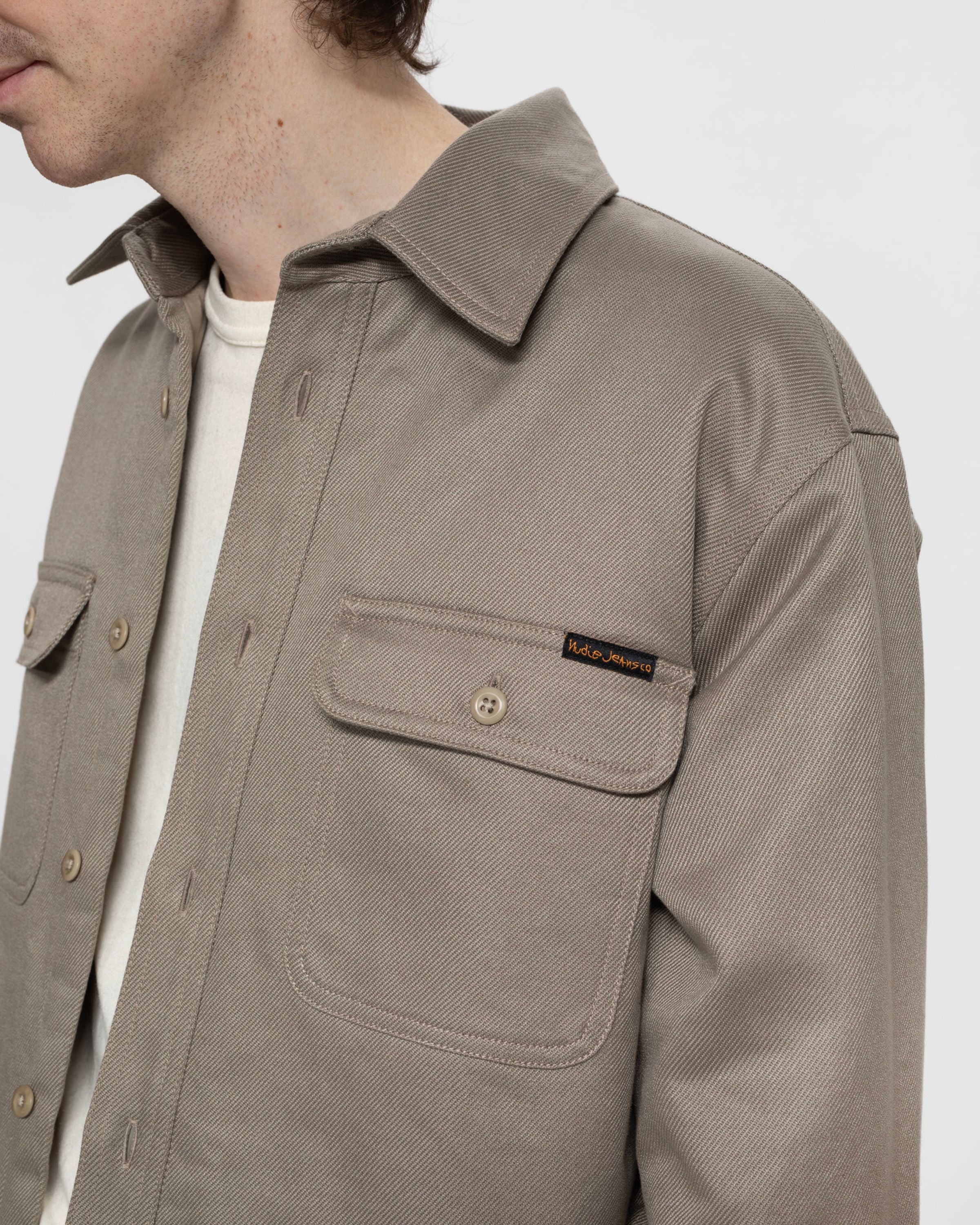 Nudie Jeans Glenn Padded Shirt in Mud, a close-up of the organic cotton twill fabric and buttoned chest pocket.