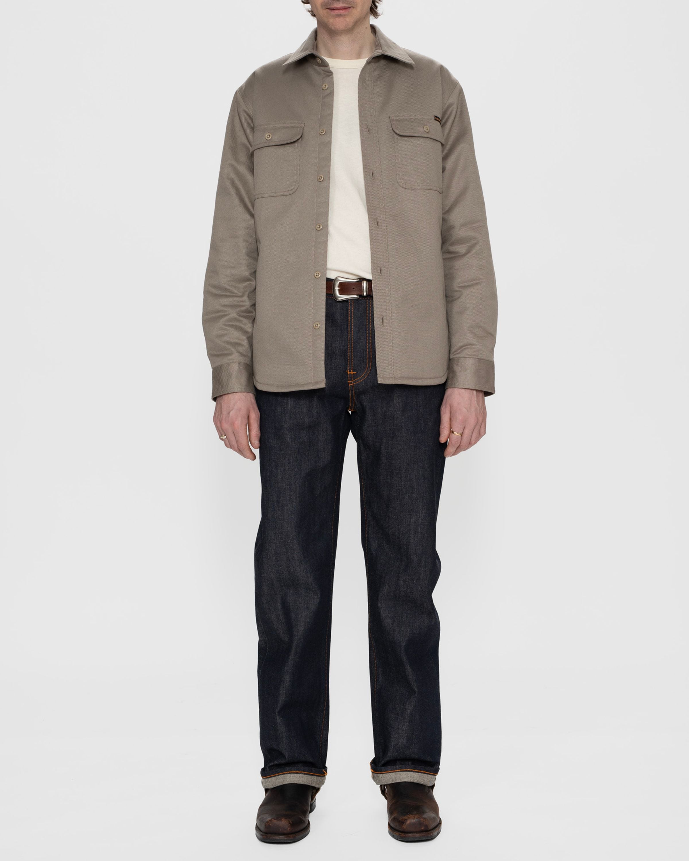 Nudie Jeans Glenn Padded Shirt in Mud, a regular fit organic cotton twill overshirt worn with dark denim jeans.