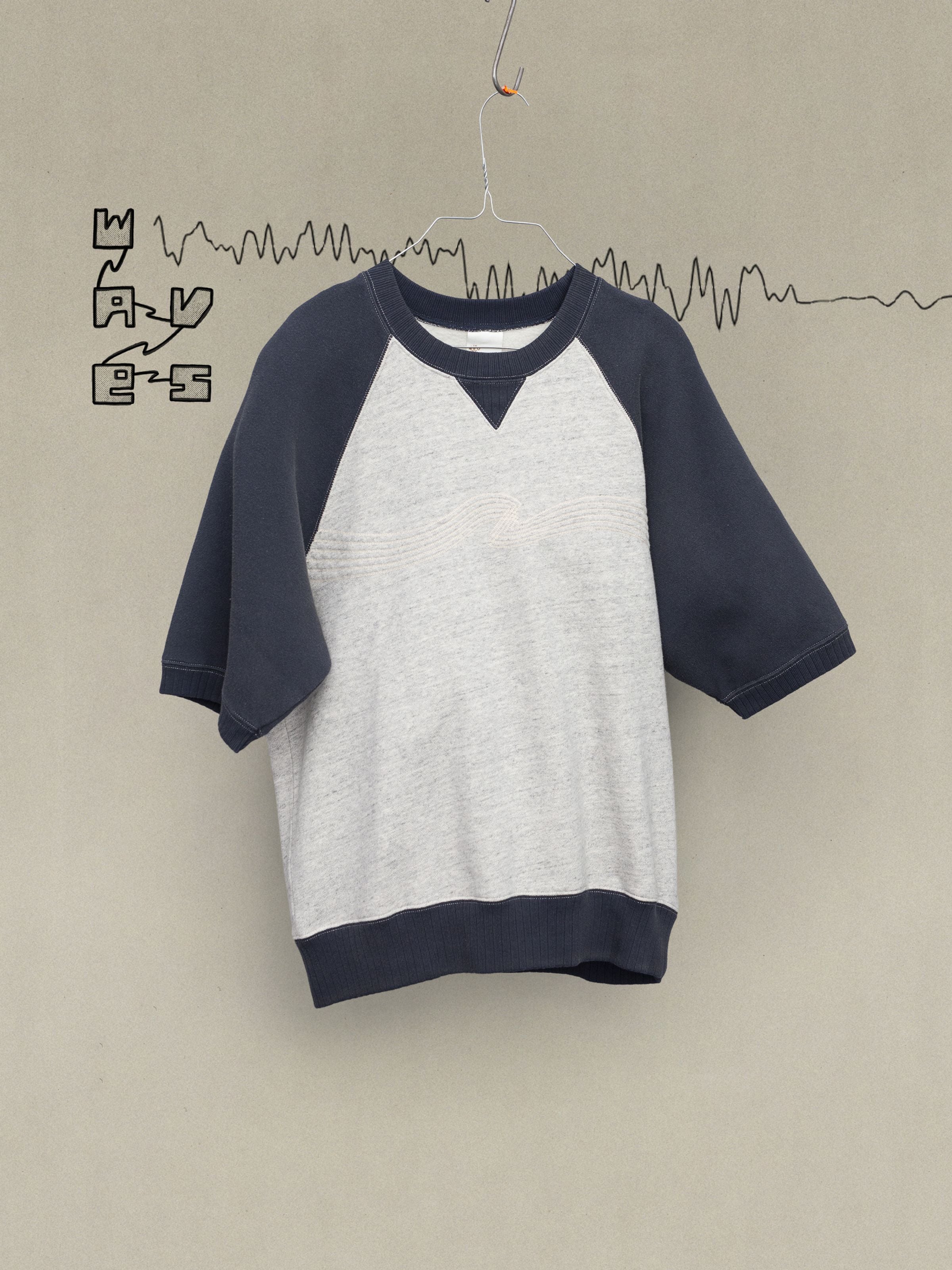 Nudie Jeans Kaj Short Sleeve Embo Wave Greymelange, an organic cotton sweatshirt with navy raglan sleeves on a hanger.