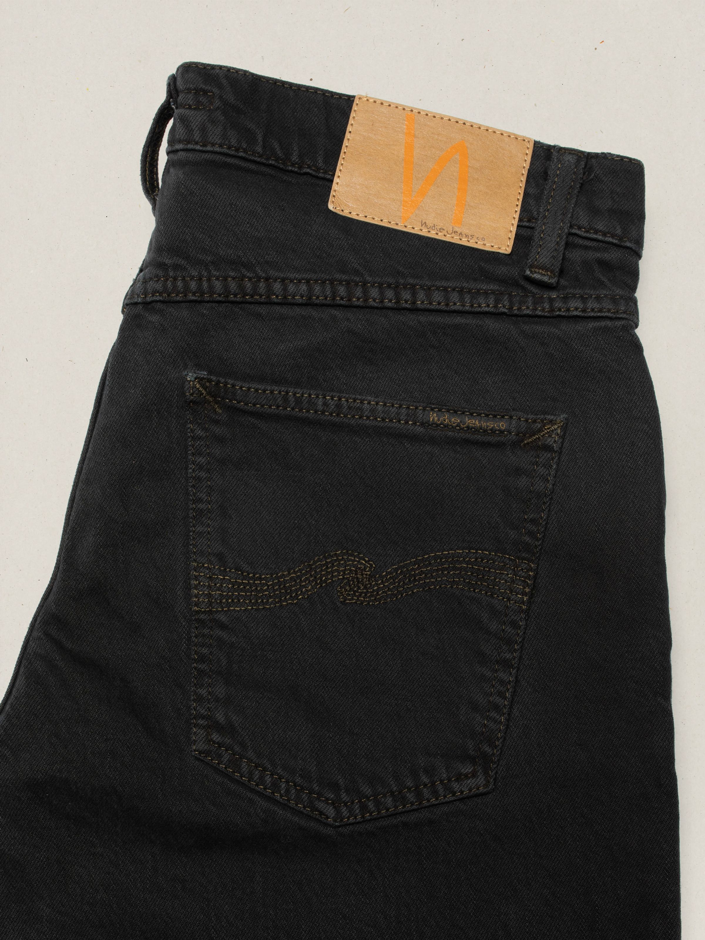 Nudie Jeans Solid Ollie Petrol Black, close-up of the back pocket and tan Jacron patch on black overdyed denim.