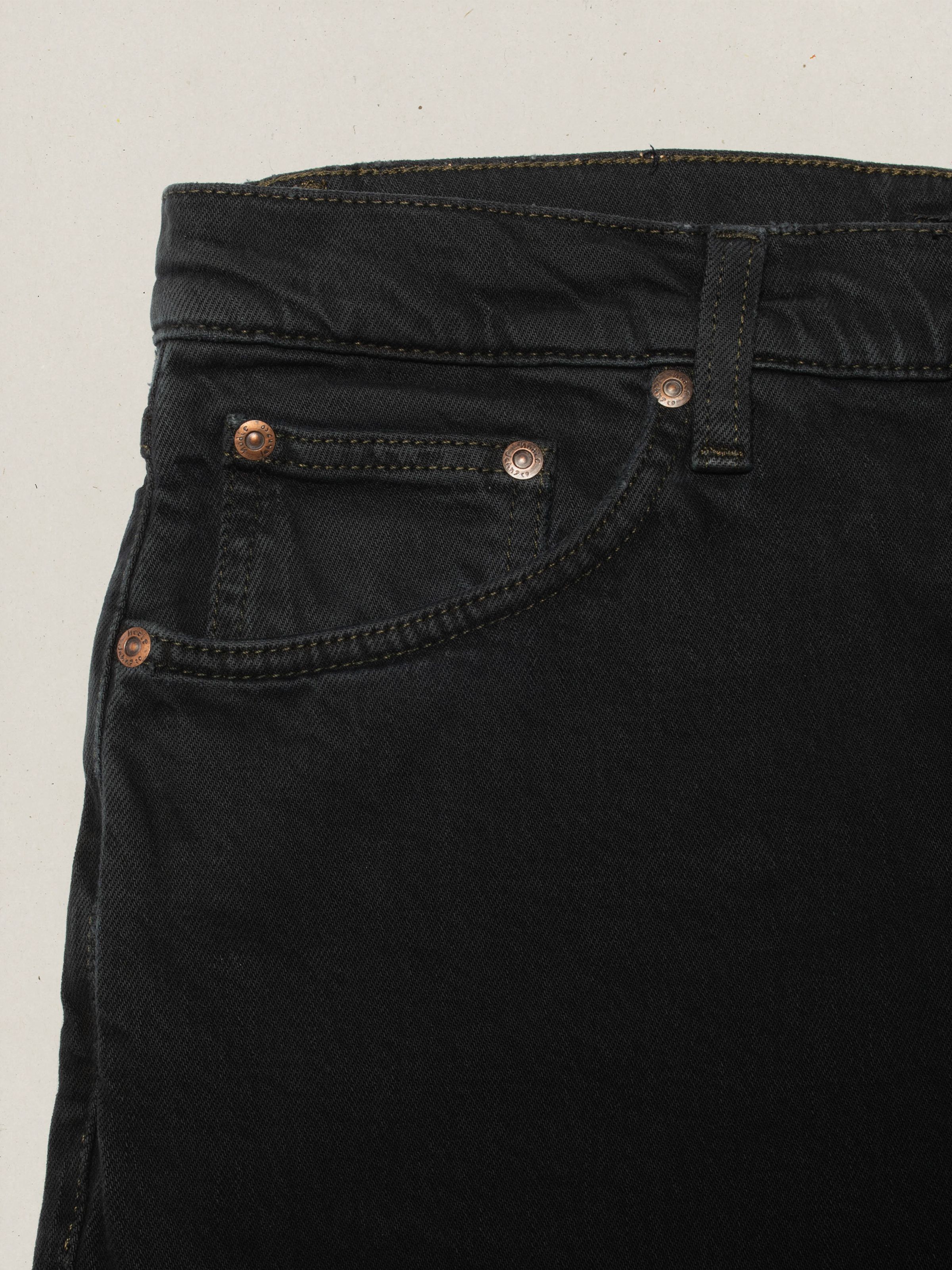 Nudie Jeans Solid Ollie Petrol Black, close-up of the front pocket and copper rivets on the overdyed black denim.