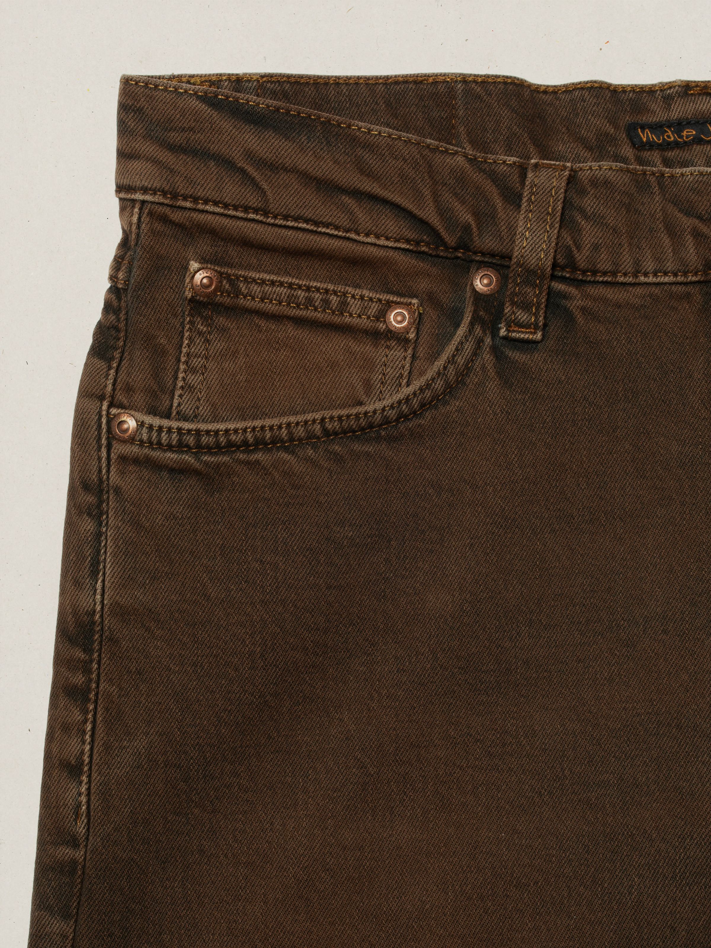 Nudie Jeans Solid Ollie Espresso Bouhlel, close-up of the front pocket and copper rivets on brown overdyed denim.