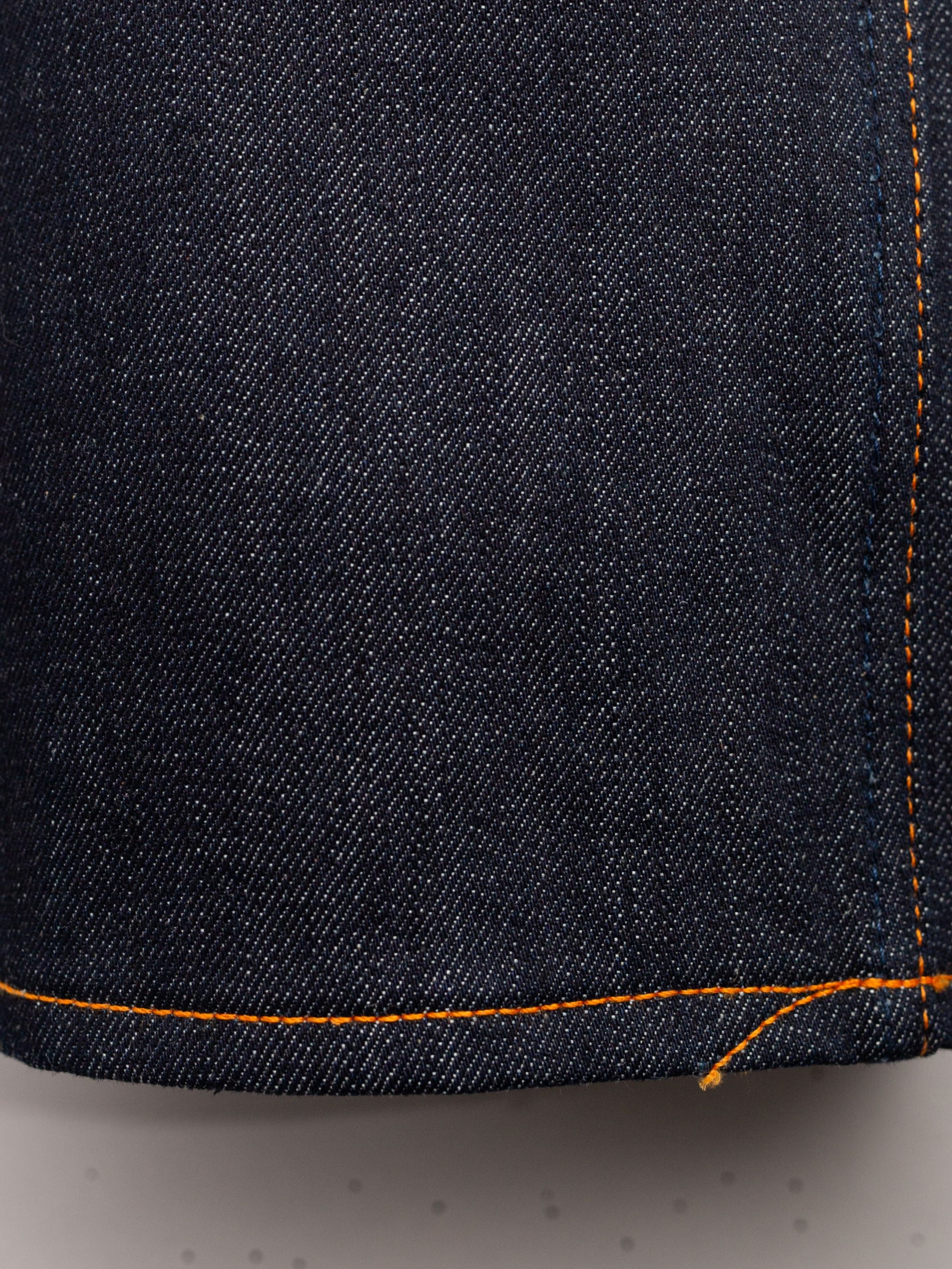 Nudie Jeans Rad Rufus Dry One, a close-up of the dark indigo rigid organic cotton denim fabric and orange hem stitch.