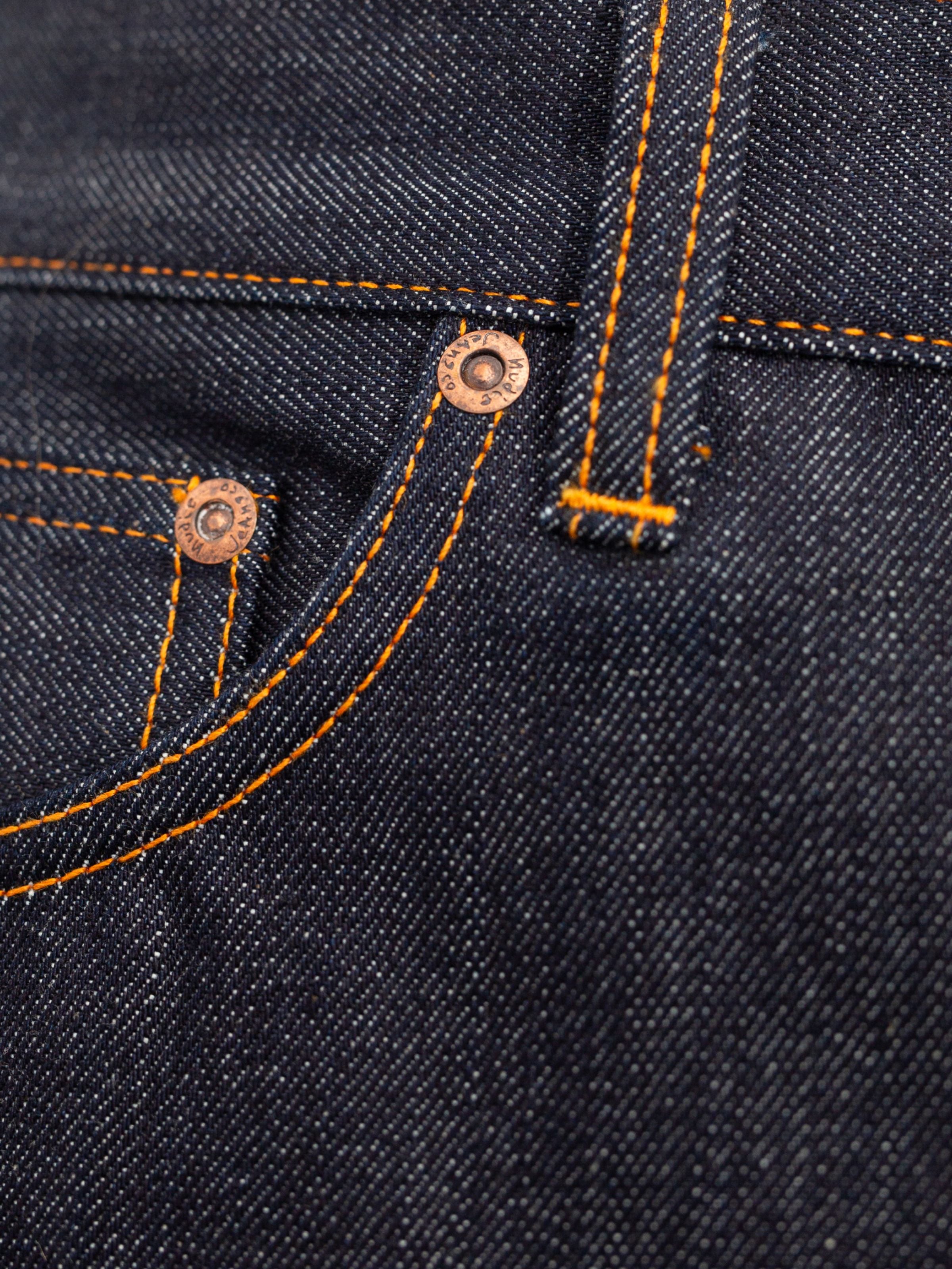 Nudie Jeans Rad Rufus Dry One, close-up of the dark indigo rigid organic cotton denim, orange thread, and copper rivets.