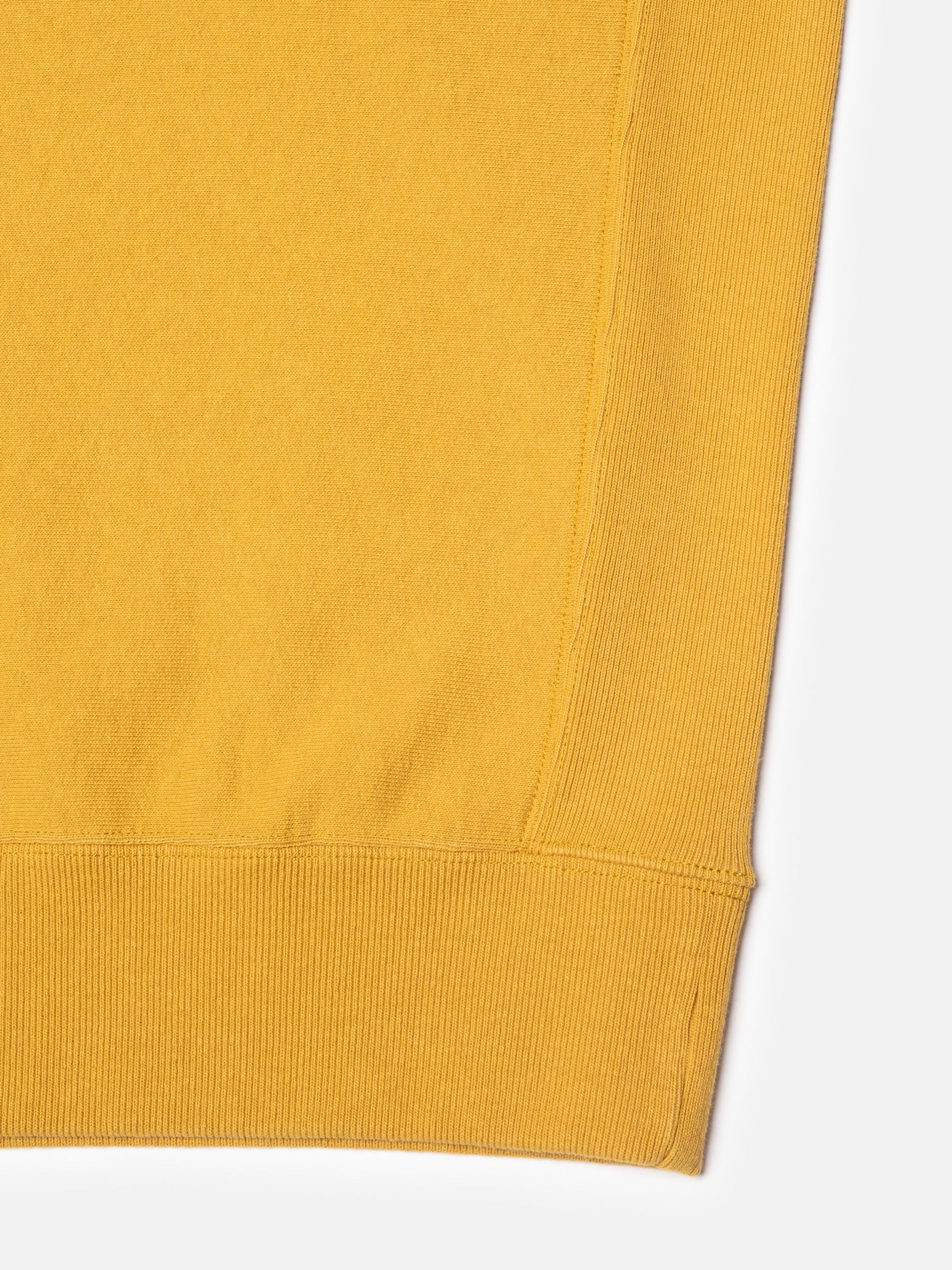 Nudie Jeans Hasse Crew Neck Sweatshirt in old yellow, showing a close-up of the heavy jersey fabric and rib insert.