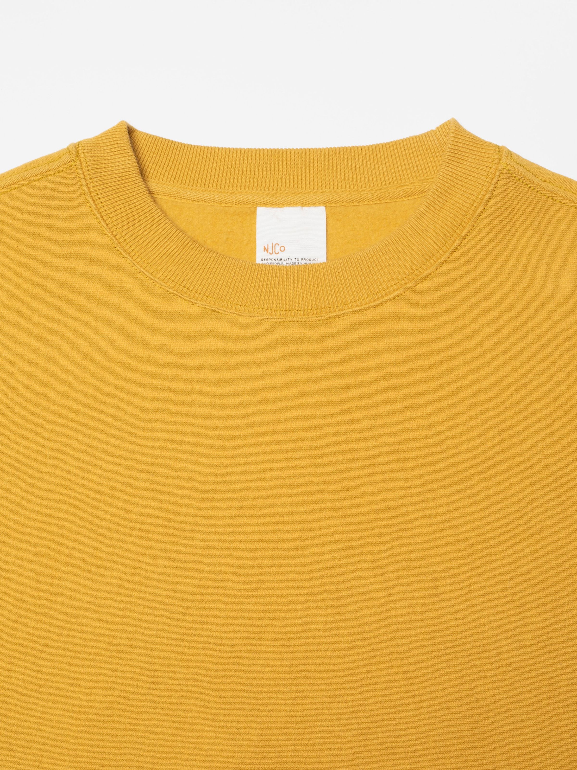 Nudie Jeans Hasse Crew Neck Sweatshirt in Old Yellow, showing a close-up of the ribbed neckline and brand label.