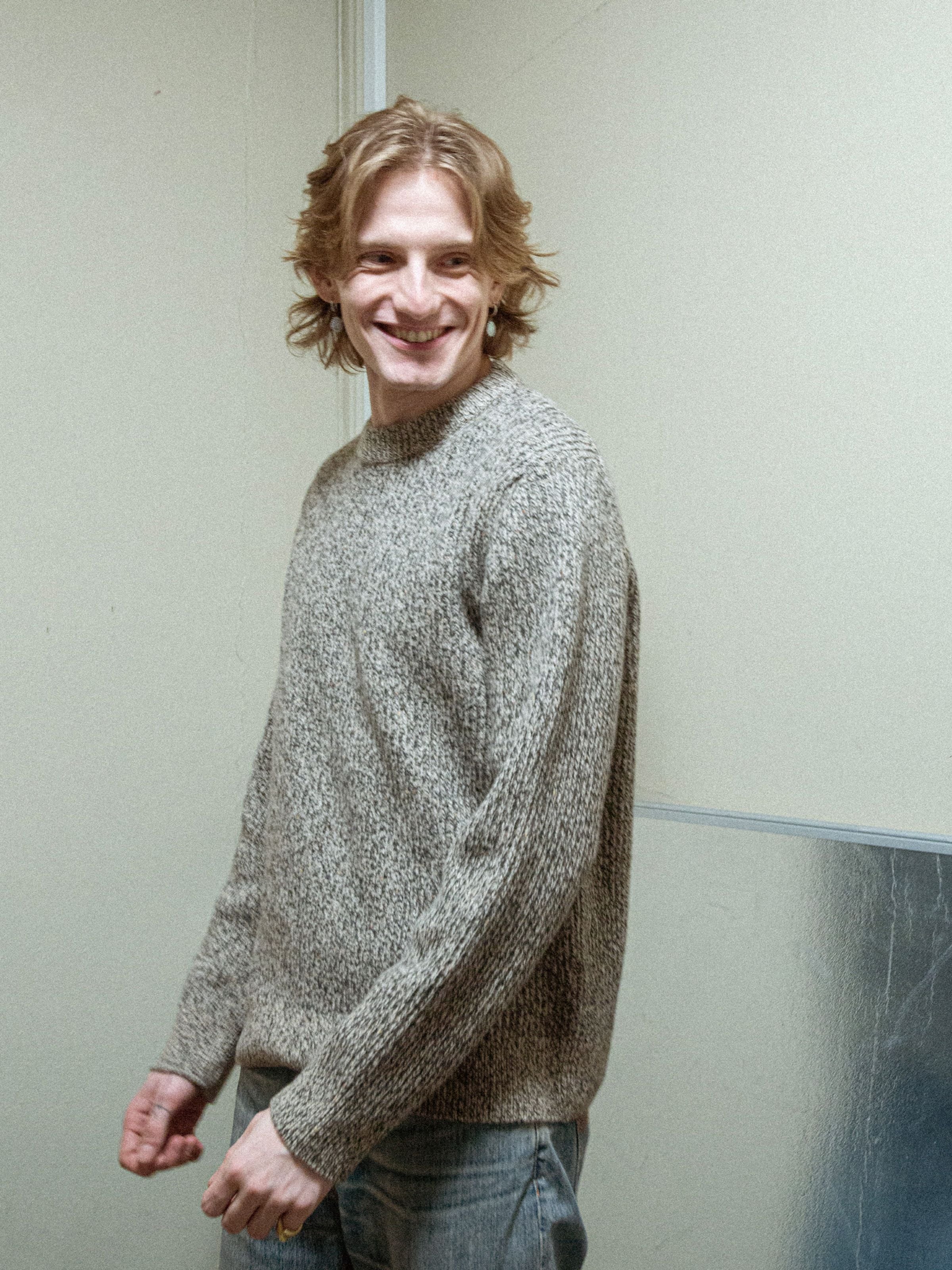 Nudie Jeans August Rib Wool Sweater in Green Melange, worn by a smiling model showcasing the textured knit.