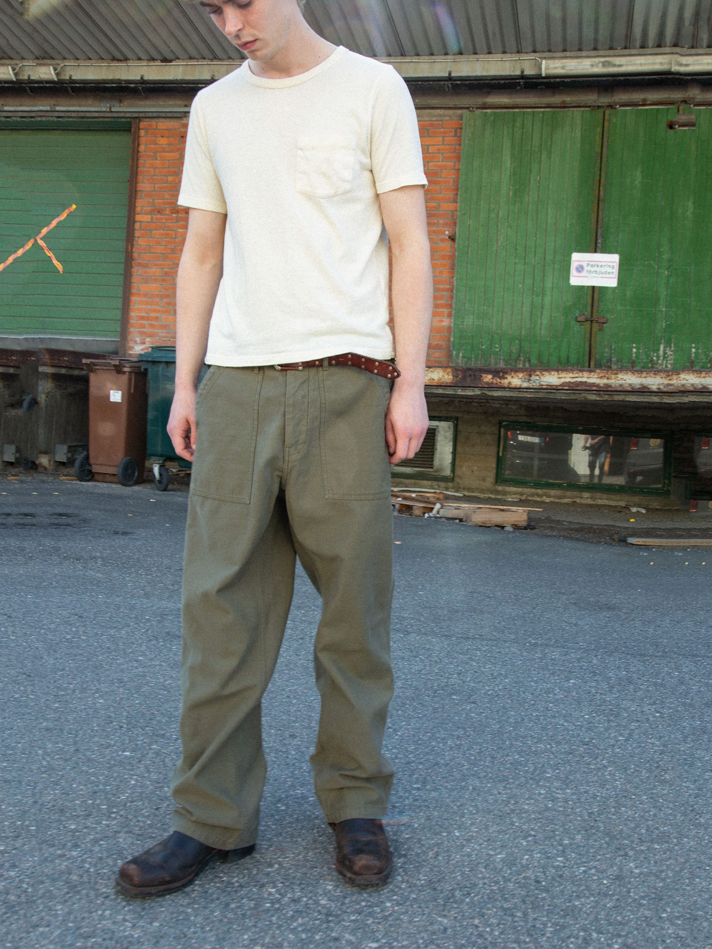 Nudie Jeans Tuff Tony Pants BS Olive Green, loose worker pants in organic cotton sateen, worn outdoors.