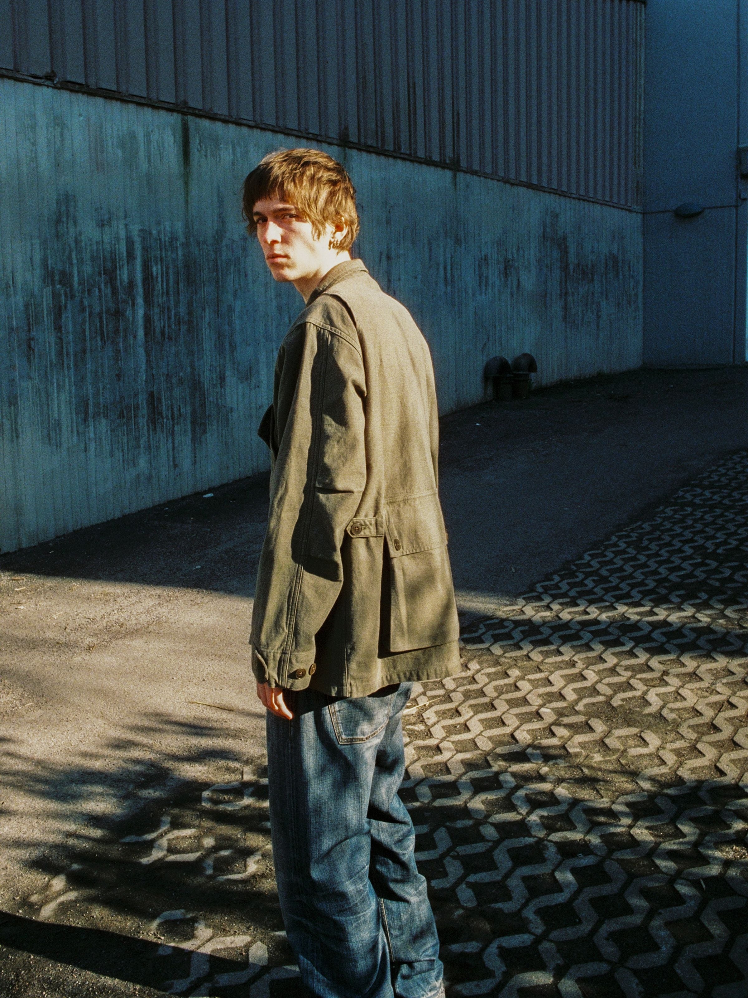 Nudie Jeans Bror Field Jacket in Olive Green, worn outdoors showing the back sateen texture and multi-pocket details.