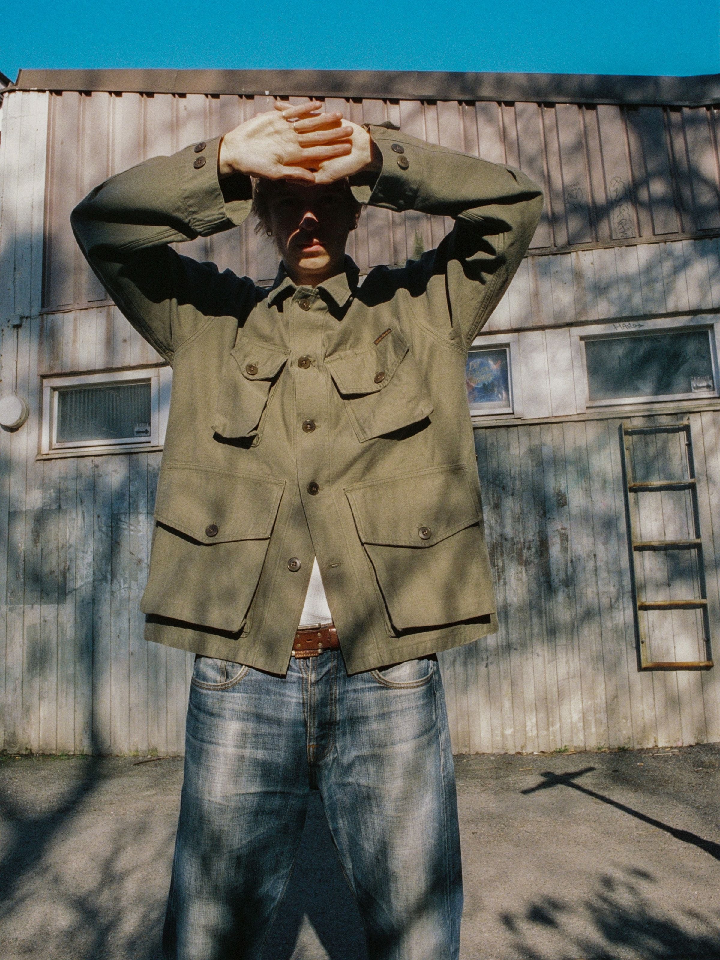 Nudie Jeans Bror Field Jacket in Olive Green, lifestyle full-length shot wearing the organic cotton sateen jacket outdoors.