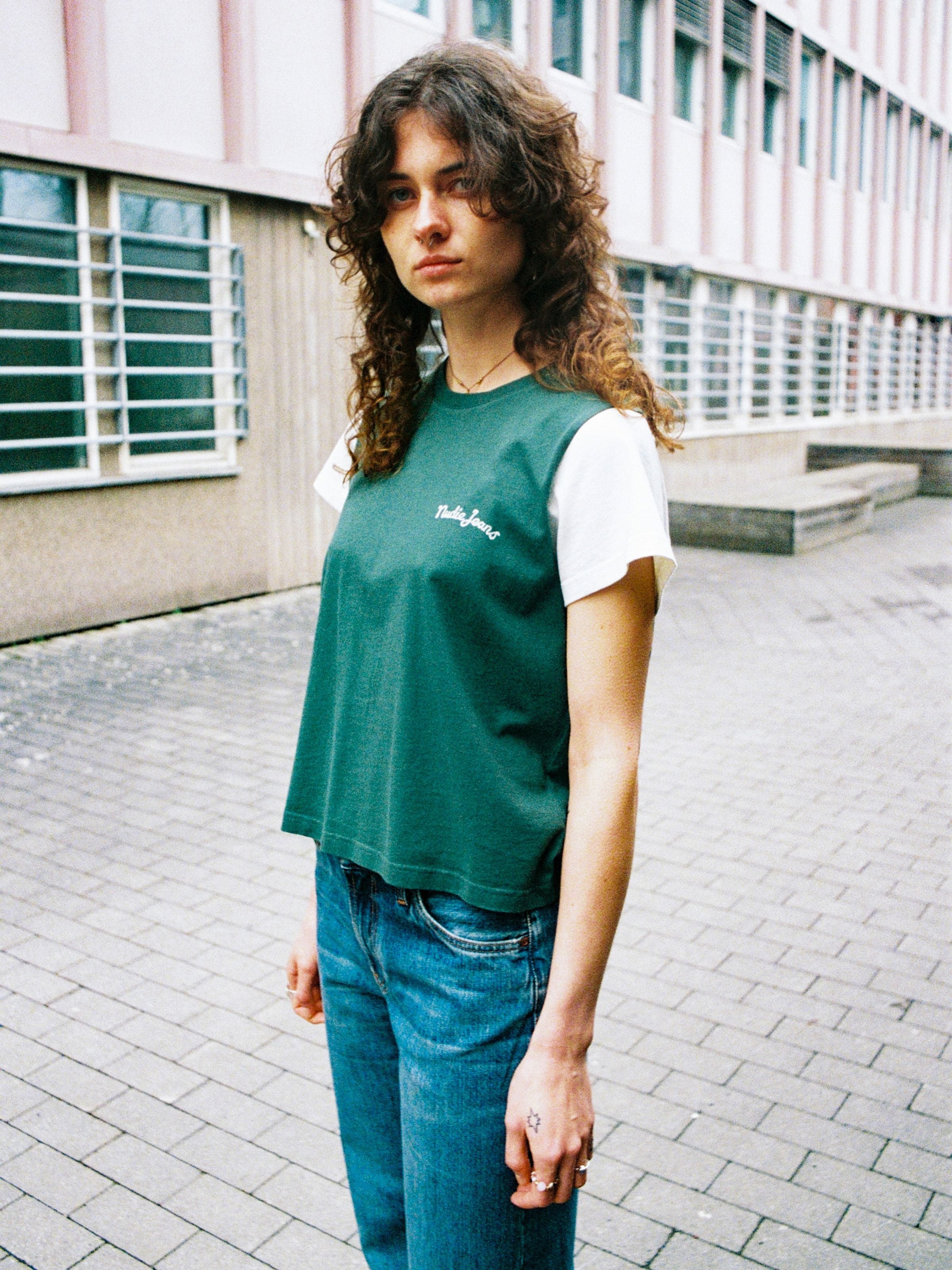 Nudie Jeans Frankie T-Shirt in Offwhite und Grün, im Freien getragen in regulärer Passform mit Kontrastärmeln.
