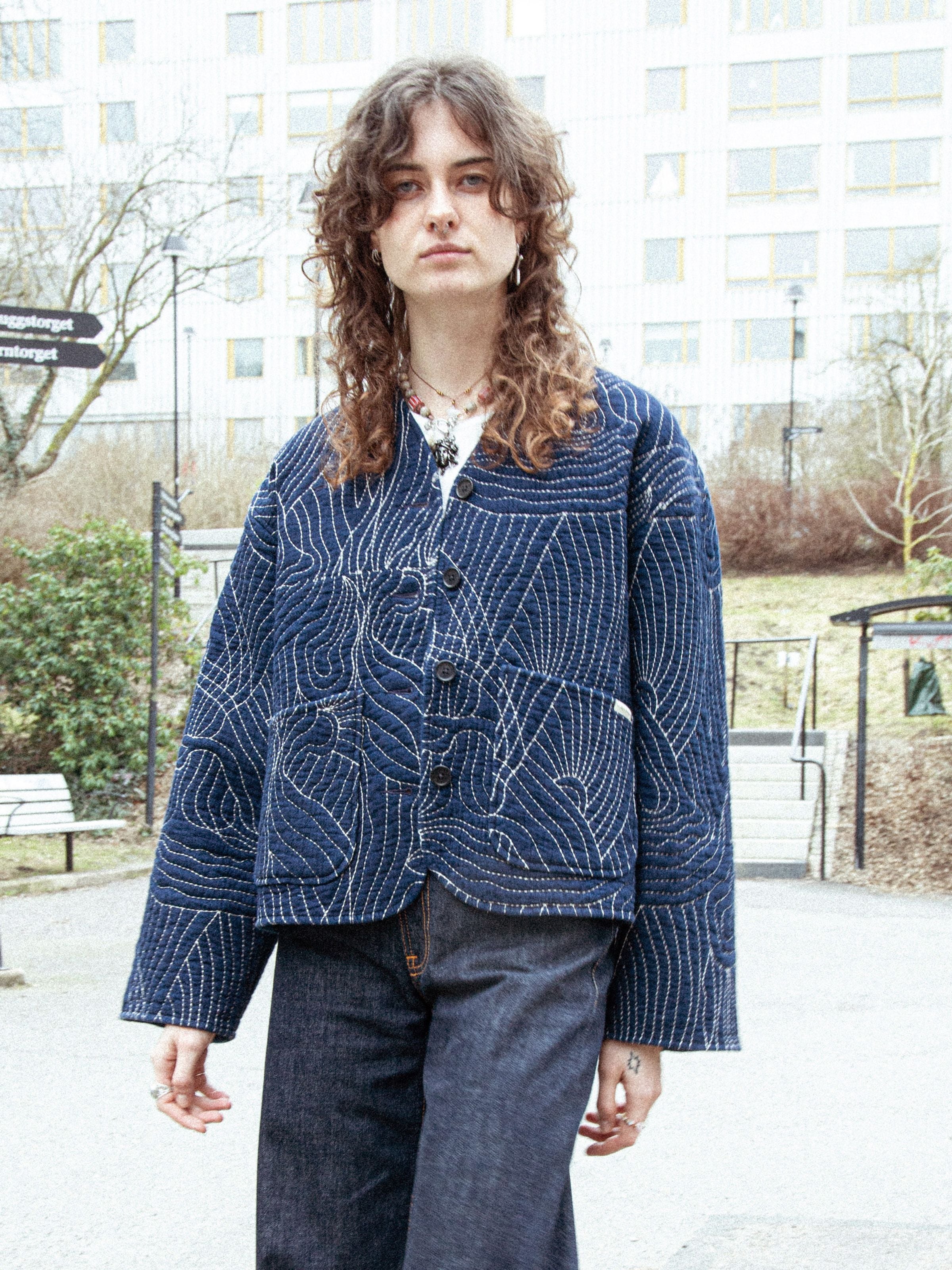 Nudie Jeans Lena Jacket Indigo Quilt in Blau, im Freien getragen, zeigt das gesteppte Muster und die lockere Passform.