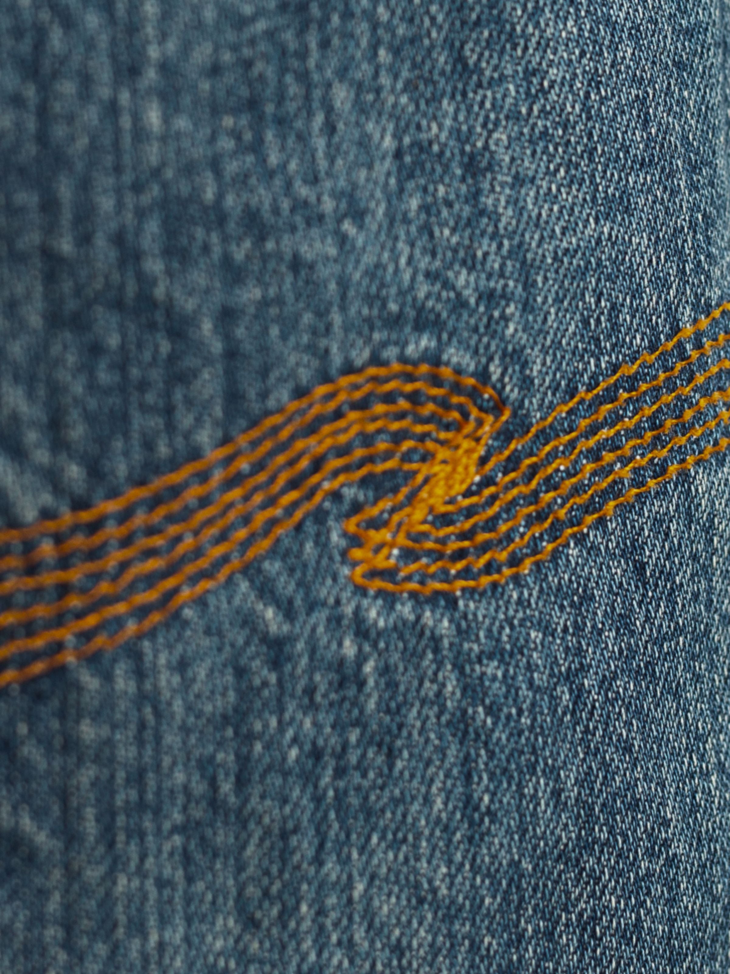 Nudie Jeans Dusty Dee Lineage Tracks, showing a close-up of the orange back pocket embroidery and washed denim texture.