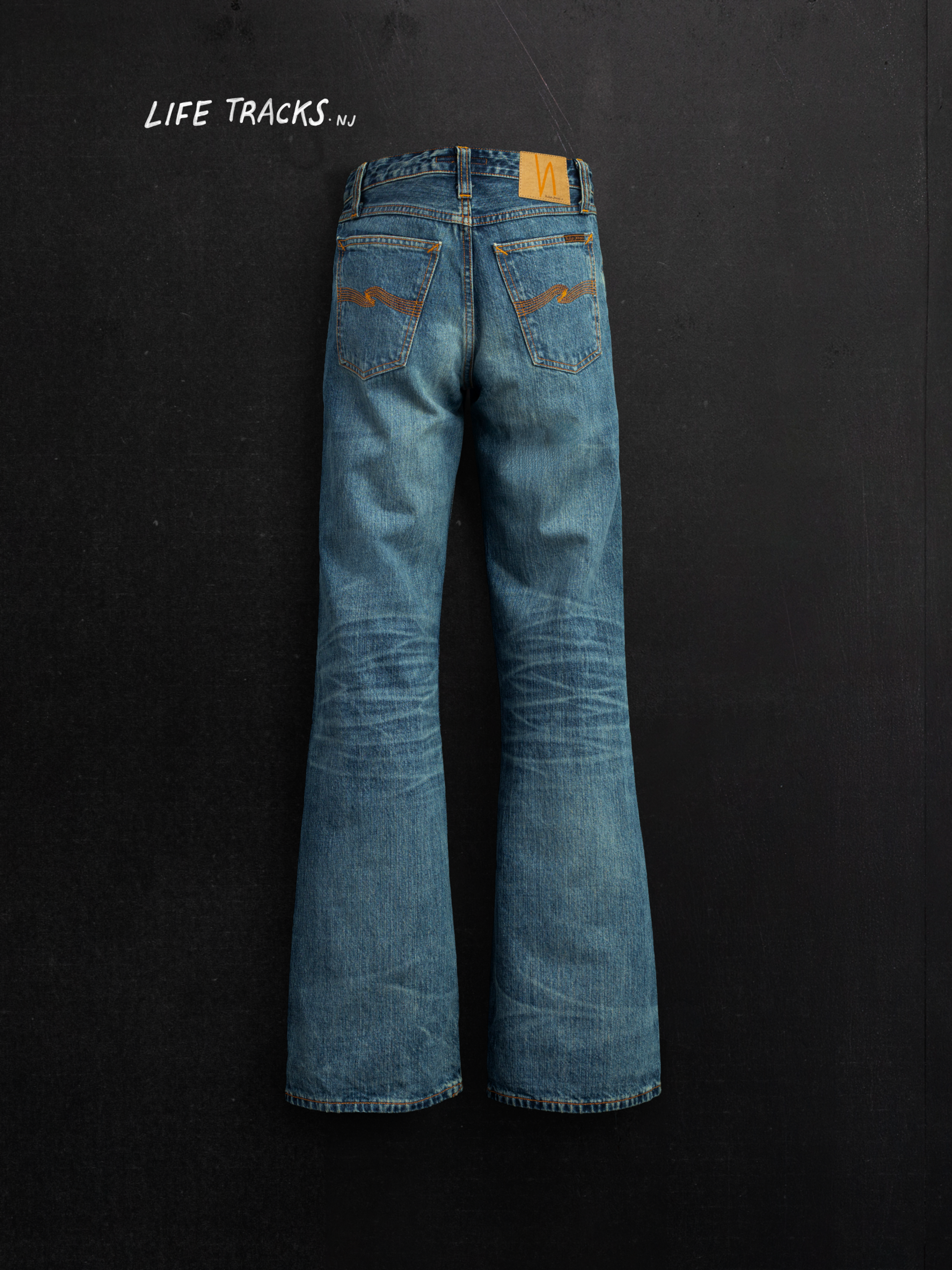 Nudie Jeans Dusty Dee Lineage Tracks, women's flared fit jeans, shown in a back view against a dark background.