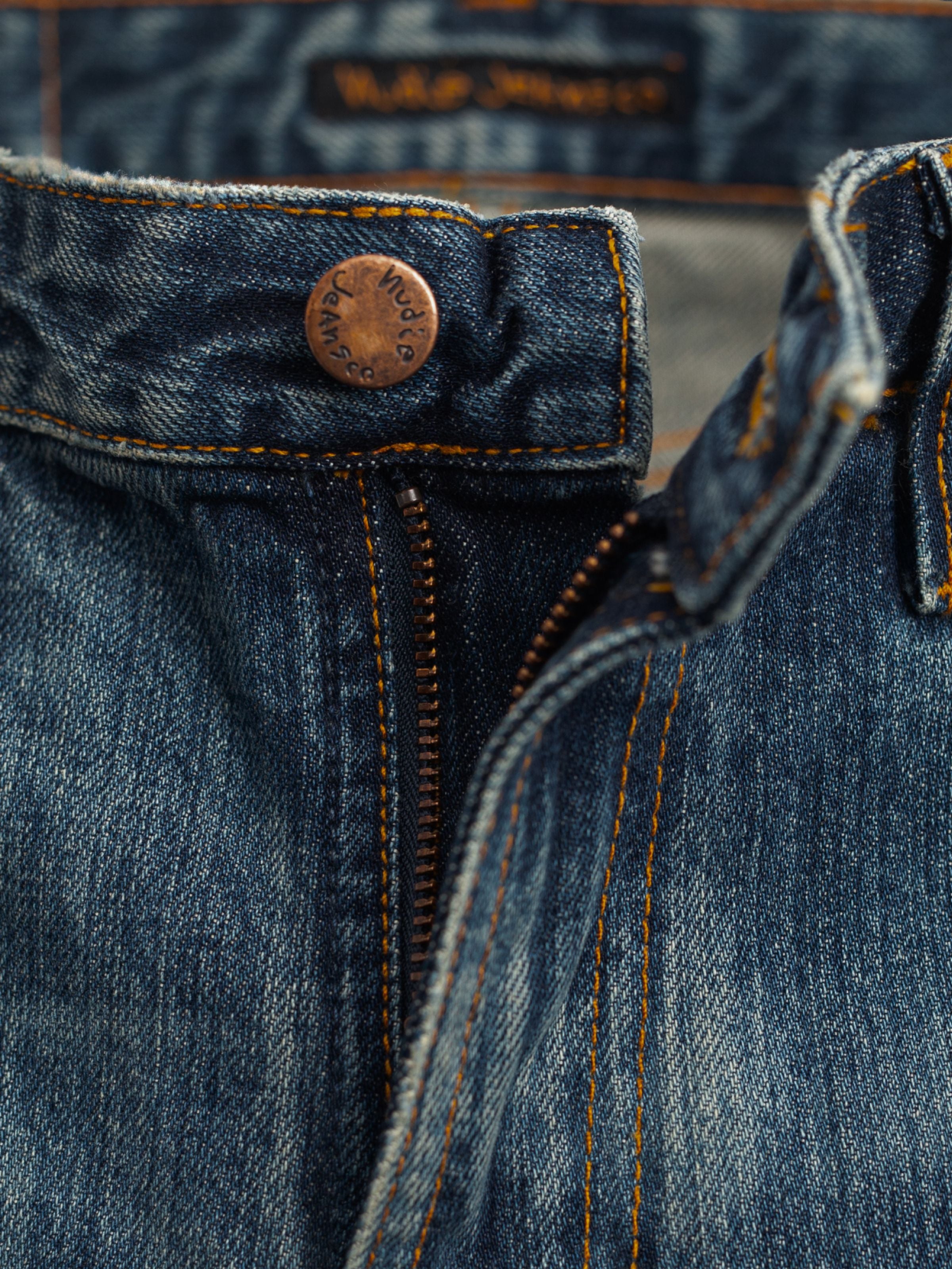 Nudie Jeans Dusty Dee Lineage Tracks, showing a close-up of the copper button, zip fly, and organic cotton denim texture.