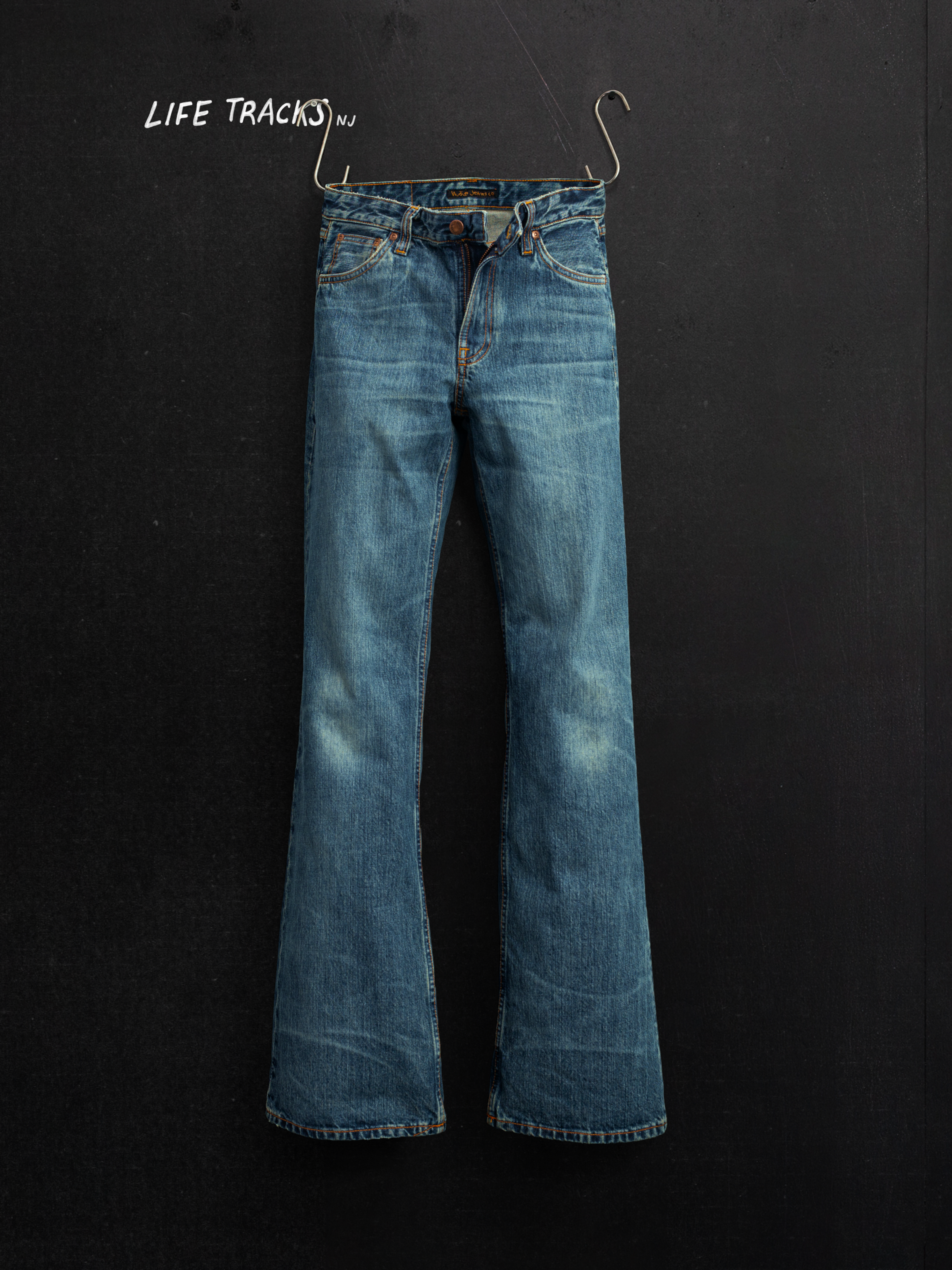 Nudie Jeans Dusty Dee Lineage Tracks, regular fit flared jeans, in a flat shot hanging against a dark background.