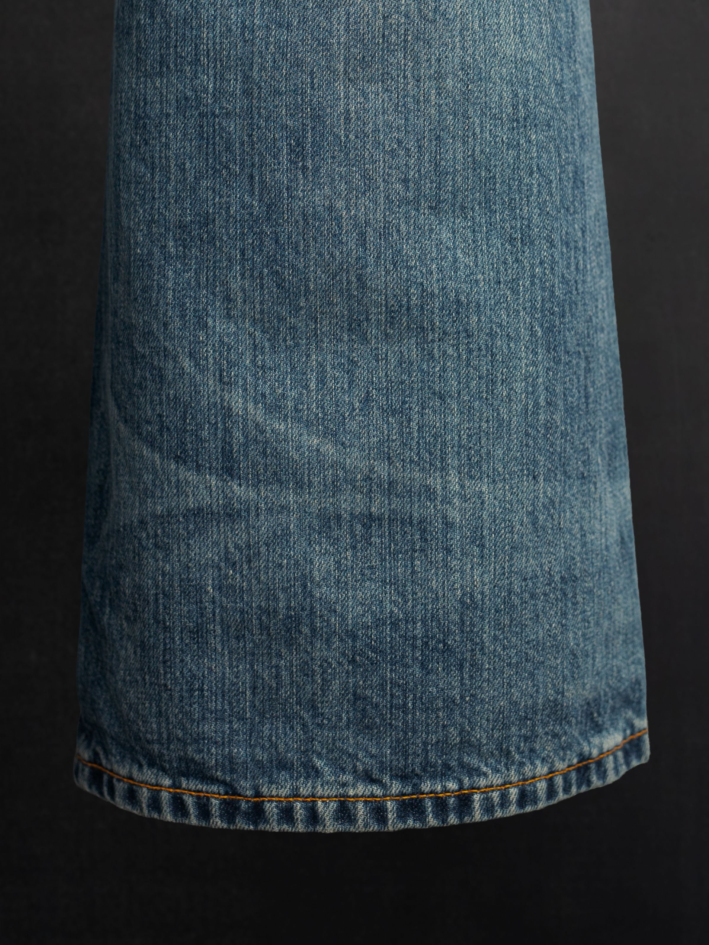 Nudie Jeans Dusty Dee Lineage Tracks, showing a close-up of the flared leg hem and textured indigo wash denim.