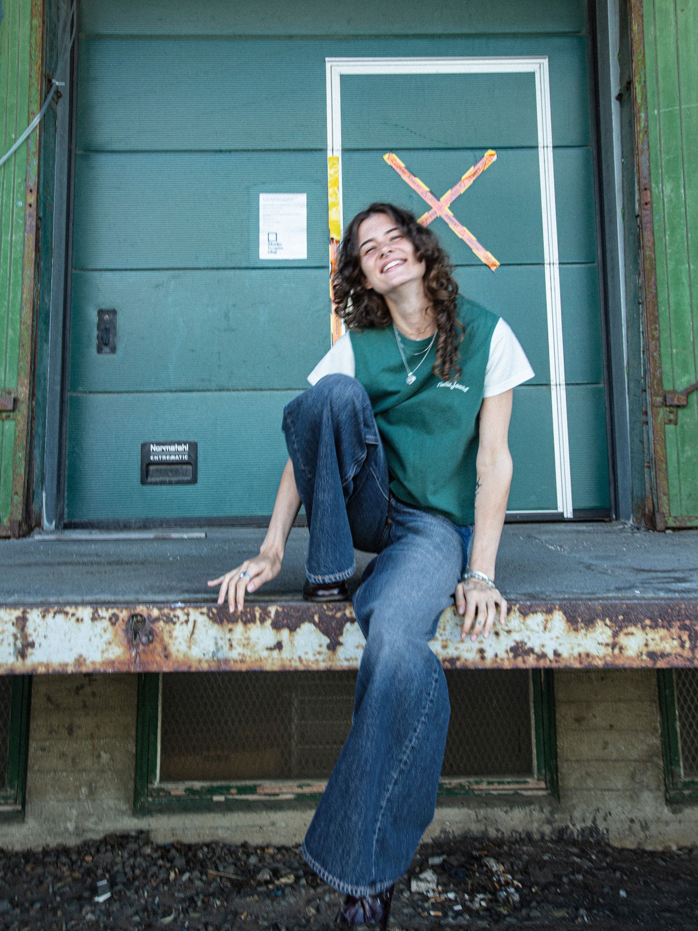 Nudie Jeans Sonic Sue Blue Poem, women's loose fit jeans in mid blue wash, worn by a model sitting outdoors.