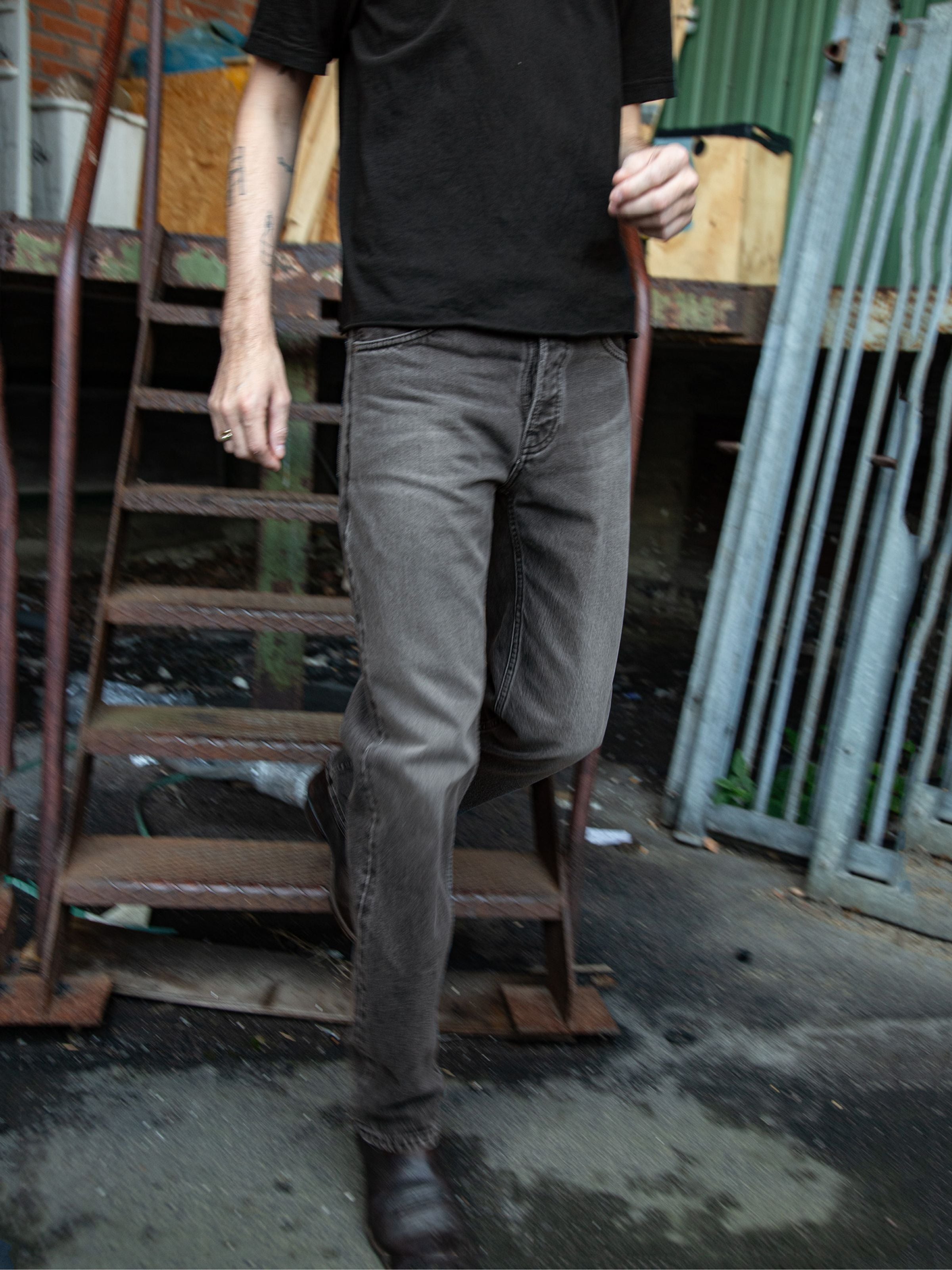 Nudie Jeans Rad Rufus Grey Lake, men's regular fit jeans in grey wash organic cotton denim, worn outdoors near metal stairs.