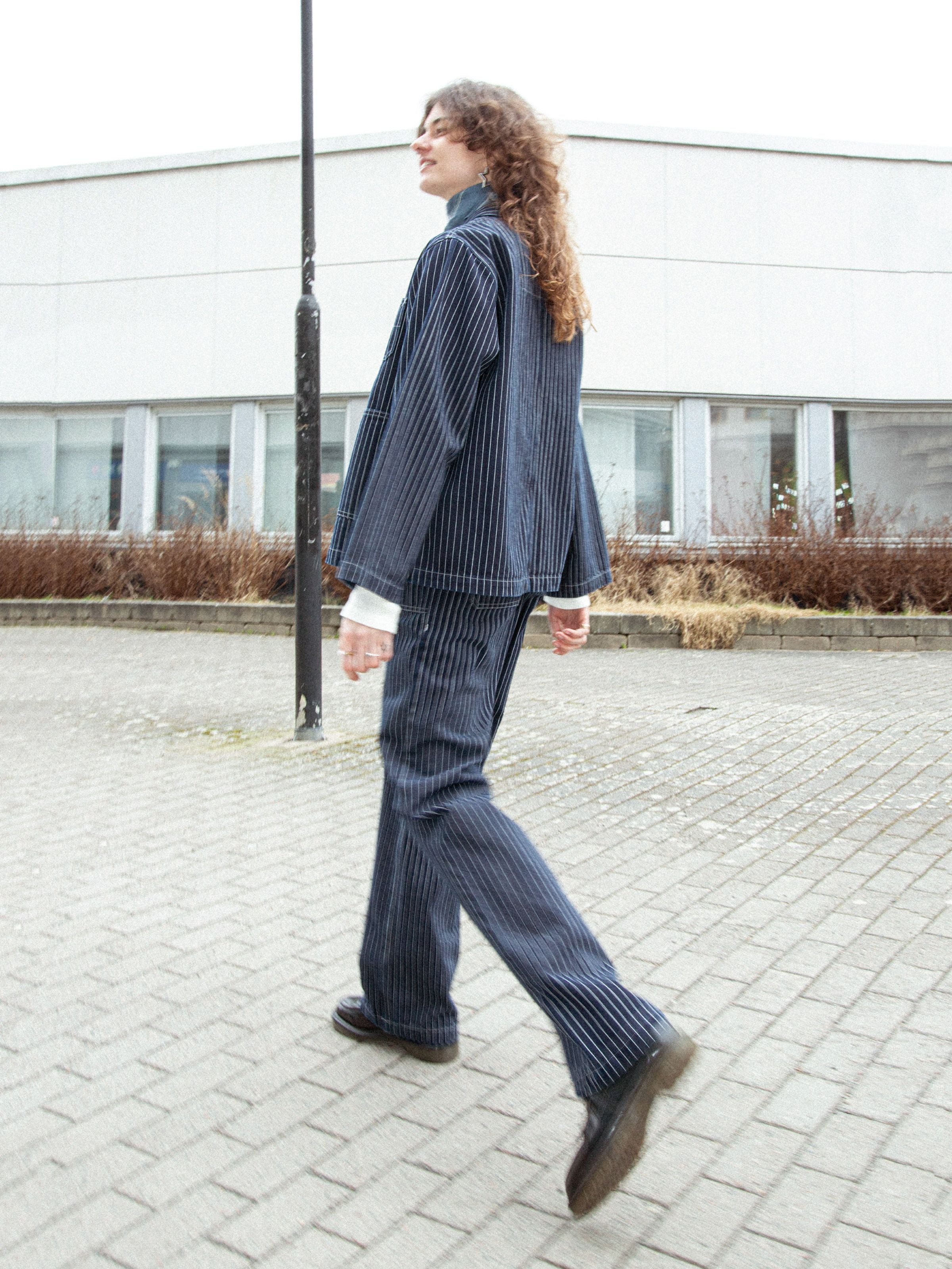 Nudie Jeans Asta Pants Pinstripe Denim, loose fit pinstripe denim pants shown worn outdoors in a full-length lifestyle shot.