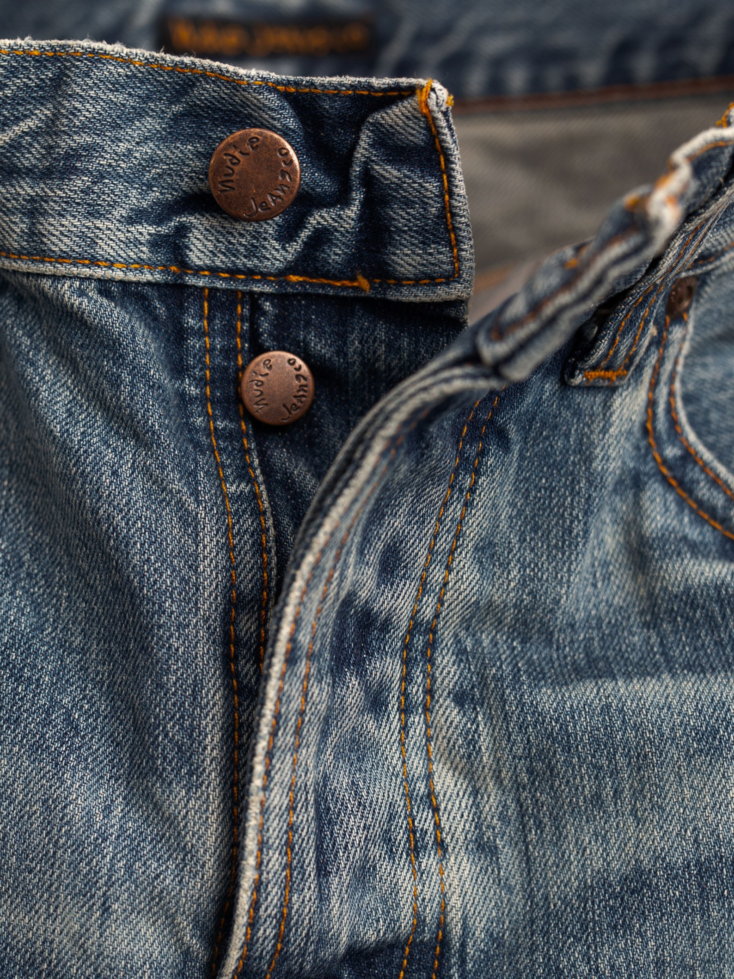 Nudie Jeans Tuff Tony Silver Tracks, Herrenjeans mit lockerer Passform, Nahaufnahme der Knopfleiste und Kupferdetails.