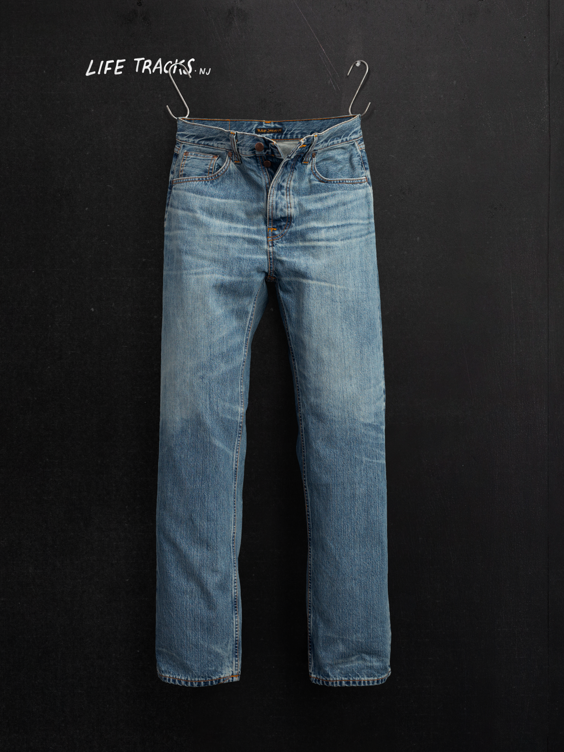 Nudie Jeans Tuff Tony Silver Tracks, Herrenjeans mit lockerer Passform, hängend vor dunklem Hintergrund.