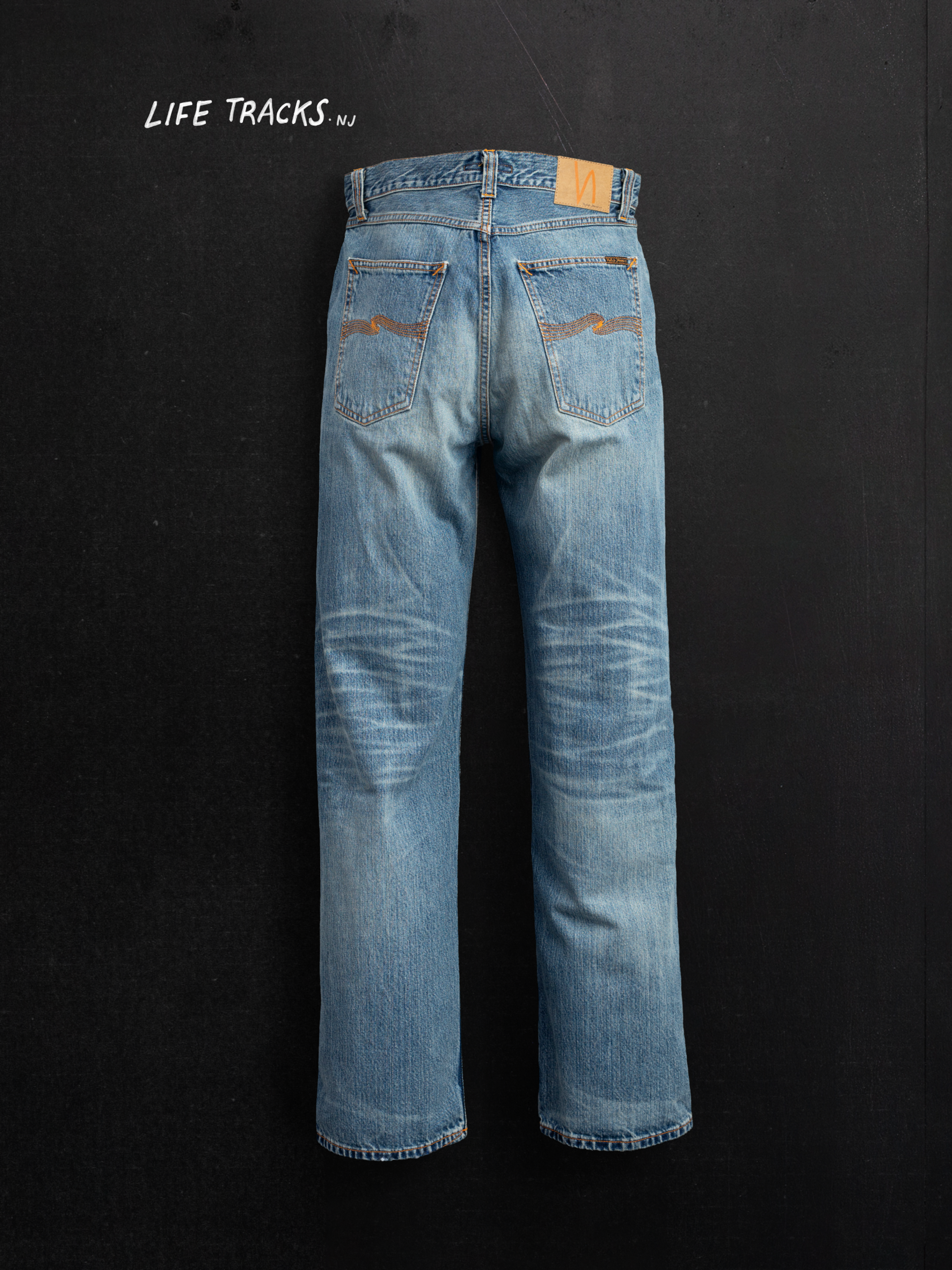 Nudie Jeans Tuff Tony Silver Tracks, Herrenjeans mit lockerer Passform von hinten vor dunklem Hintergrund.