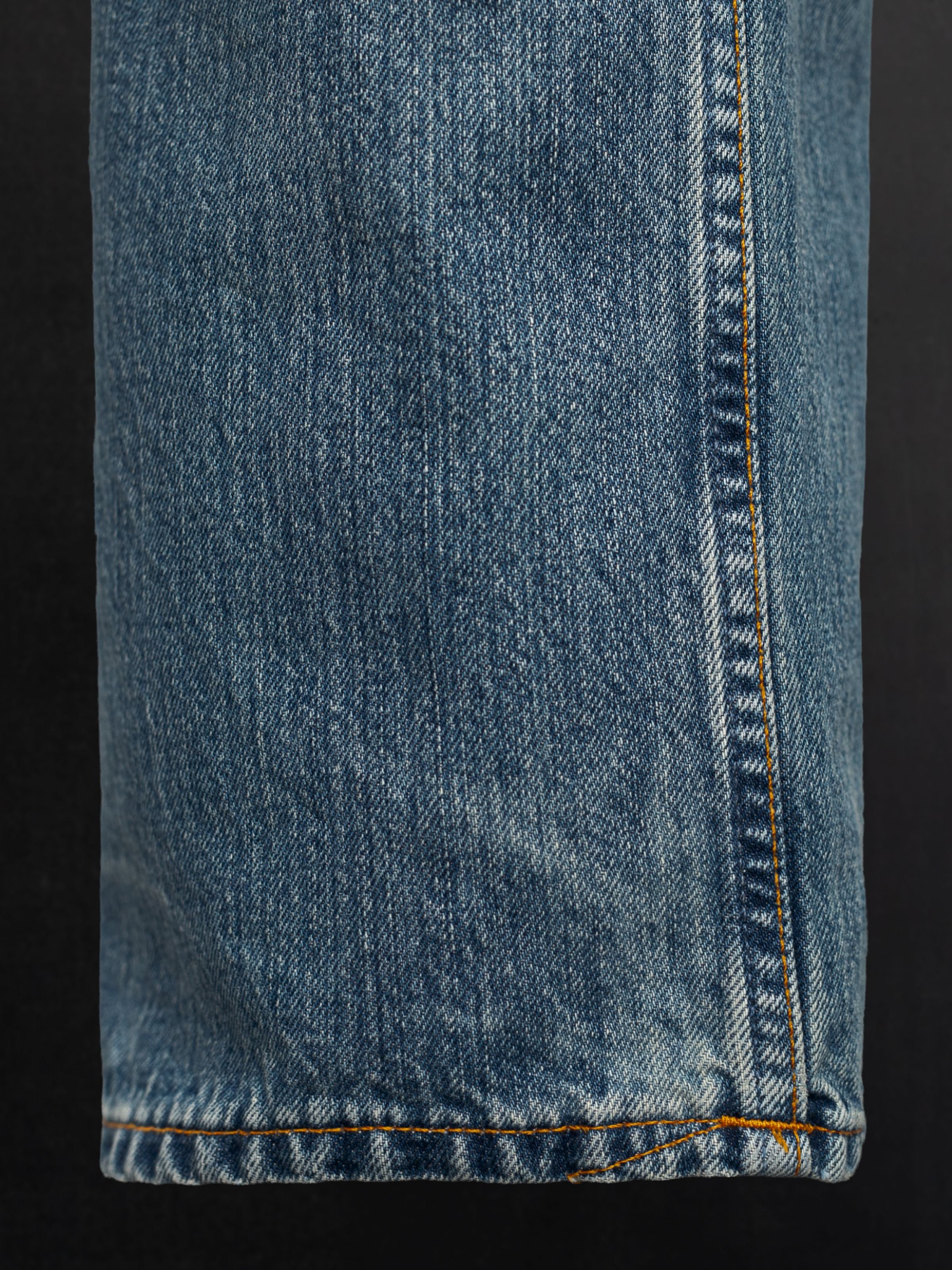 Nudie Jeans Tuff Tony Silver Tracks, Herrenjeans mit lockerer Passform, Nahaufnahme des Beinsaums und der Denim-Textur.