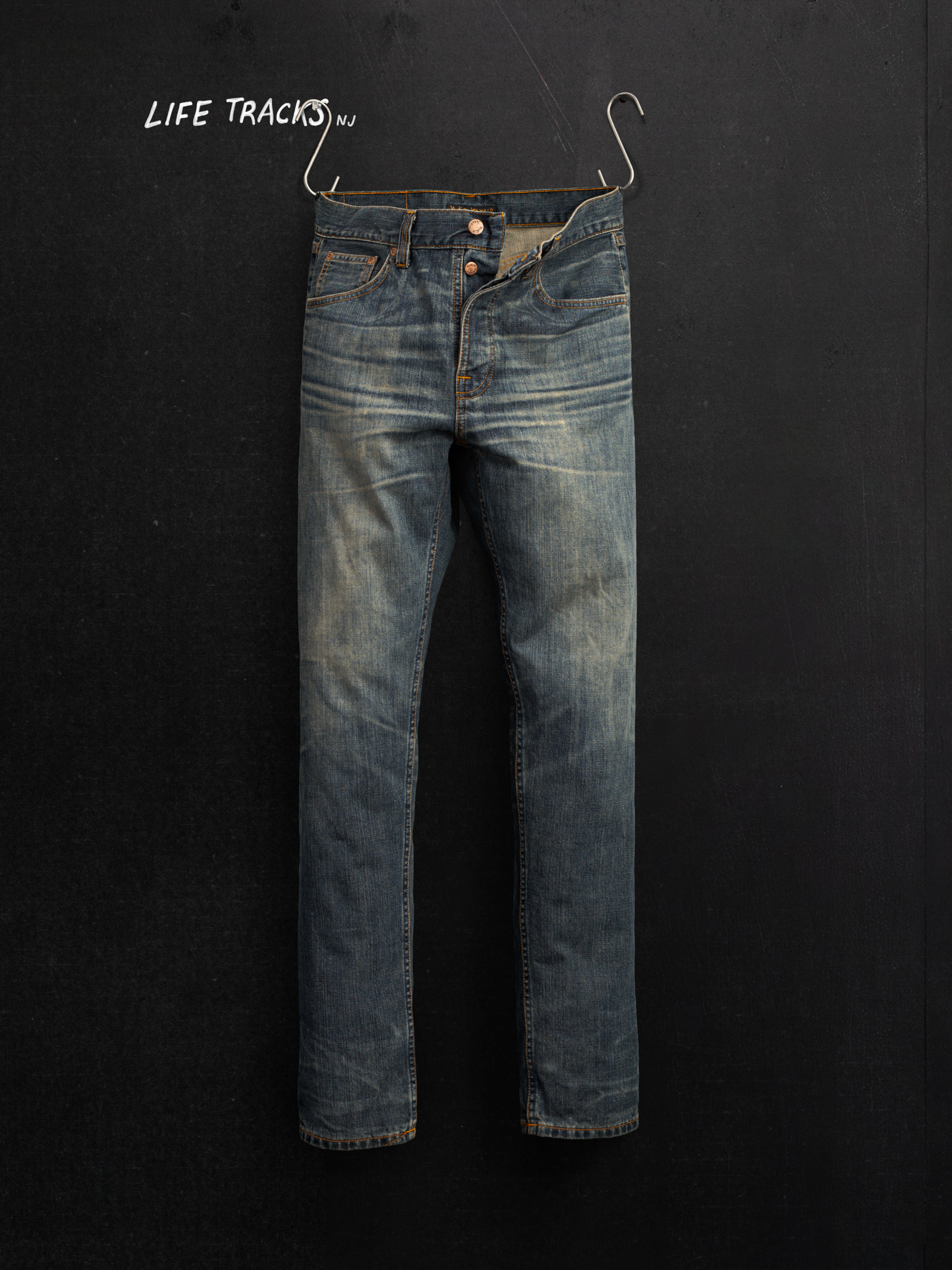 Nudie Jeans Steady Eddie II Quarter Tracks, men's regular fit jeans in dark blue wash, shown hanging on dark background.
