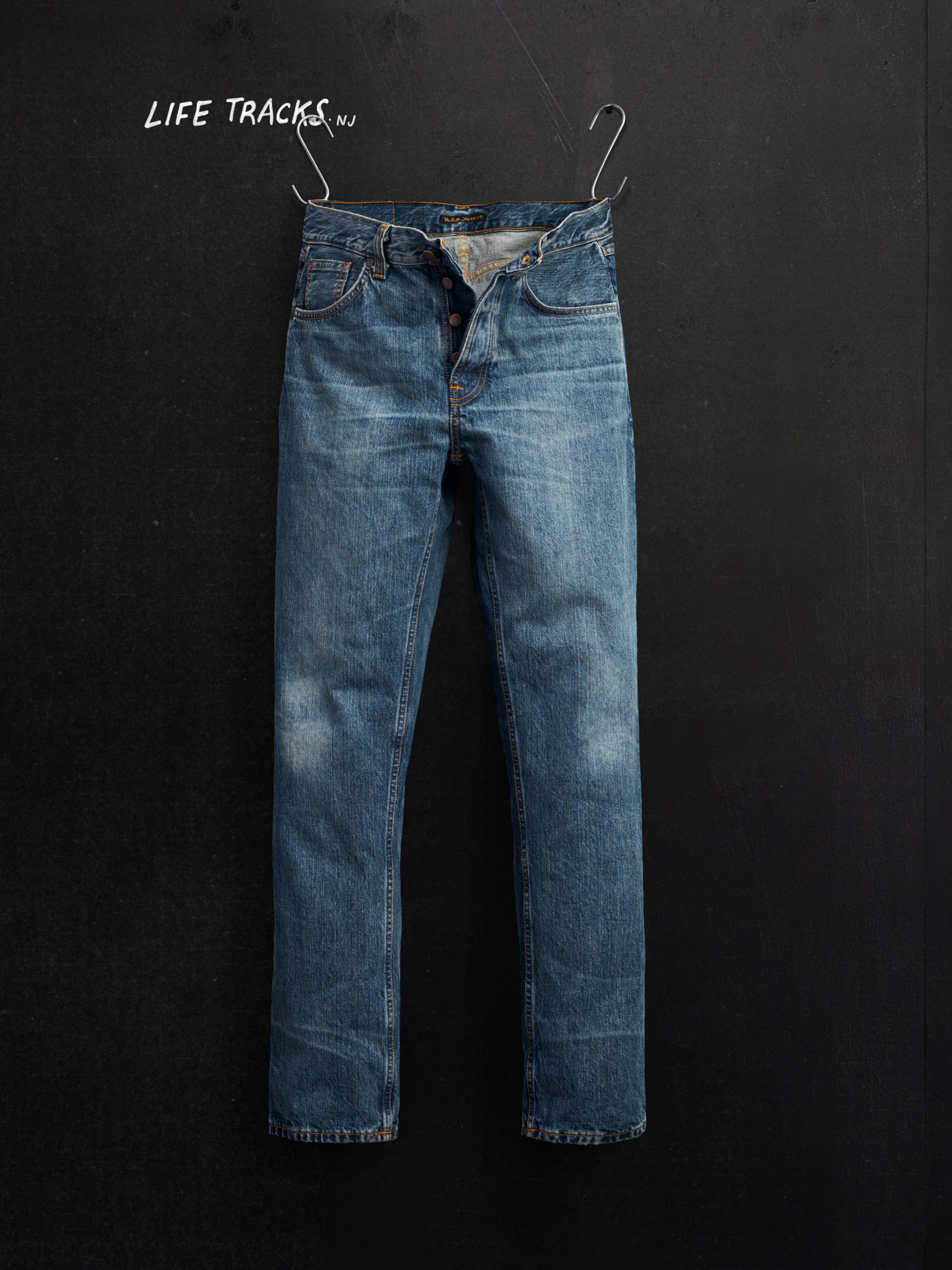 Nudie Jeans Rad Rufus Lineage Tracks, men's loose fit jeans, shown in a flat shot hanging against a dark background.