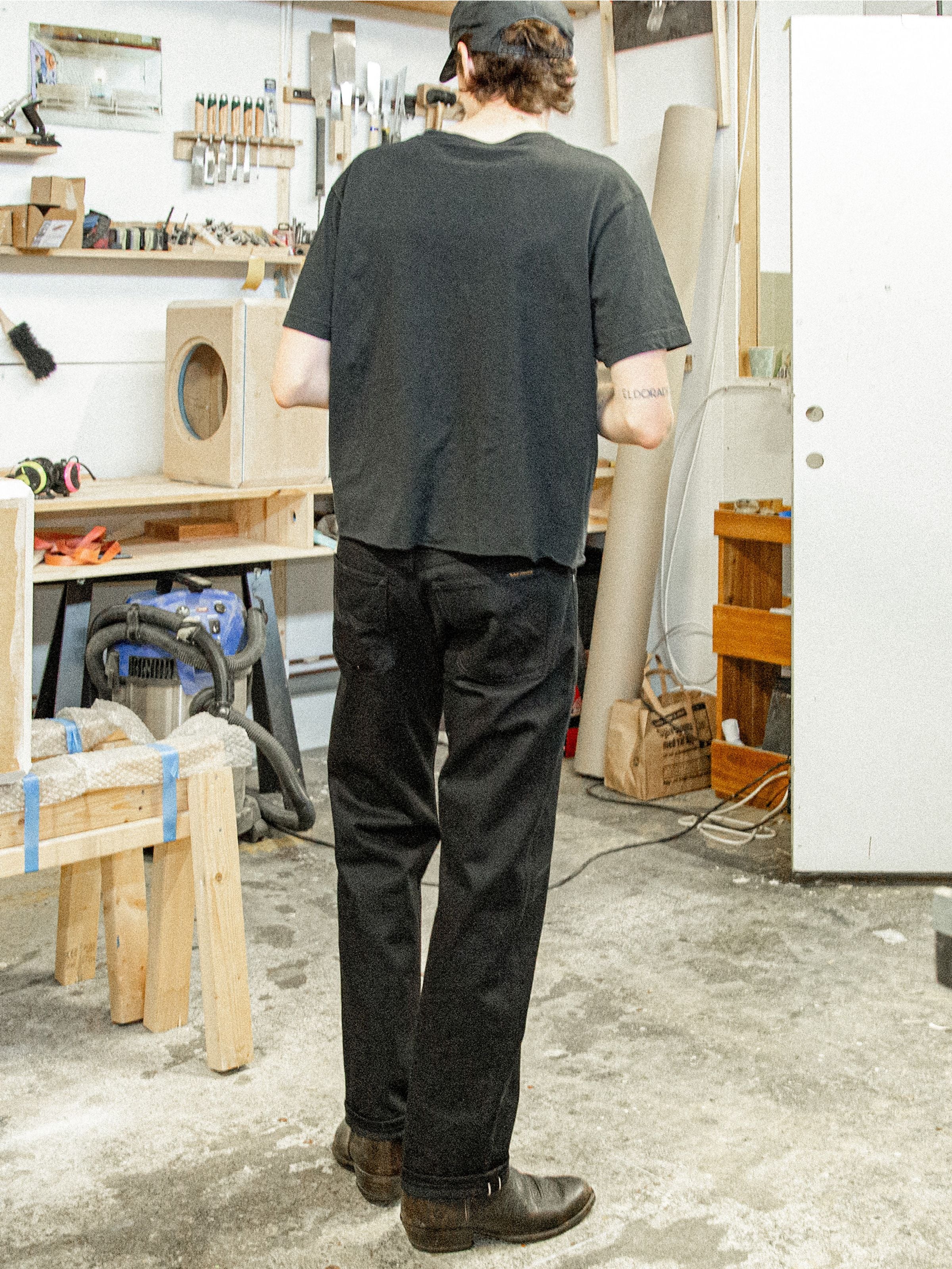 Nudie Jeans Rad Rufus Space Black Selvedge, regular-fit jeans in black shown from the back in a lifestyle workshop setting.