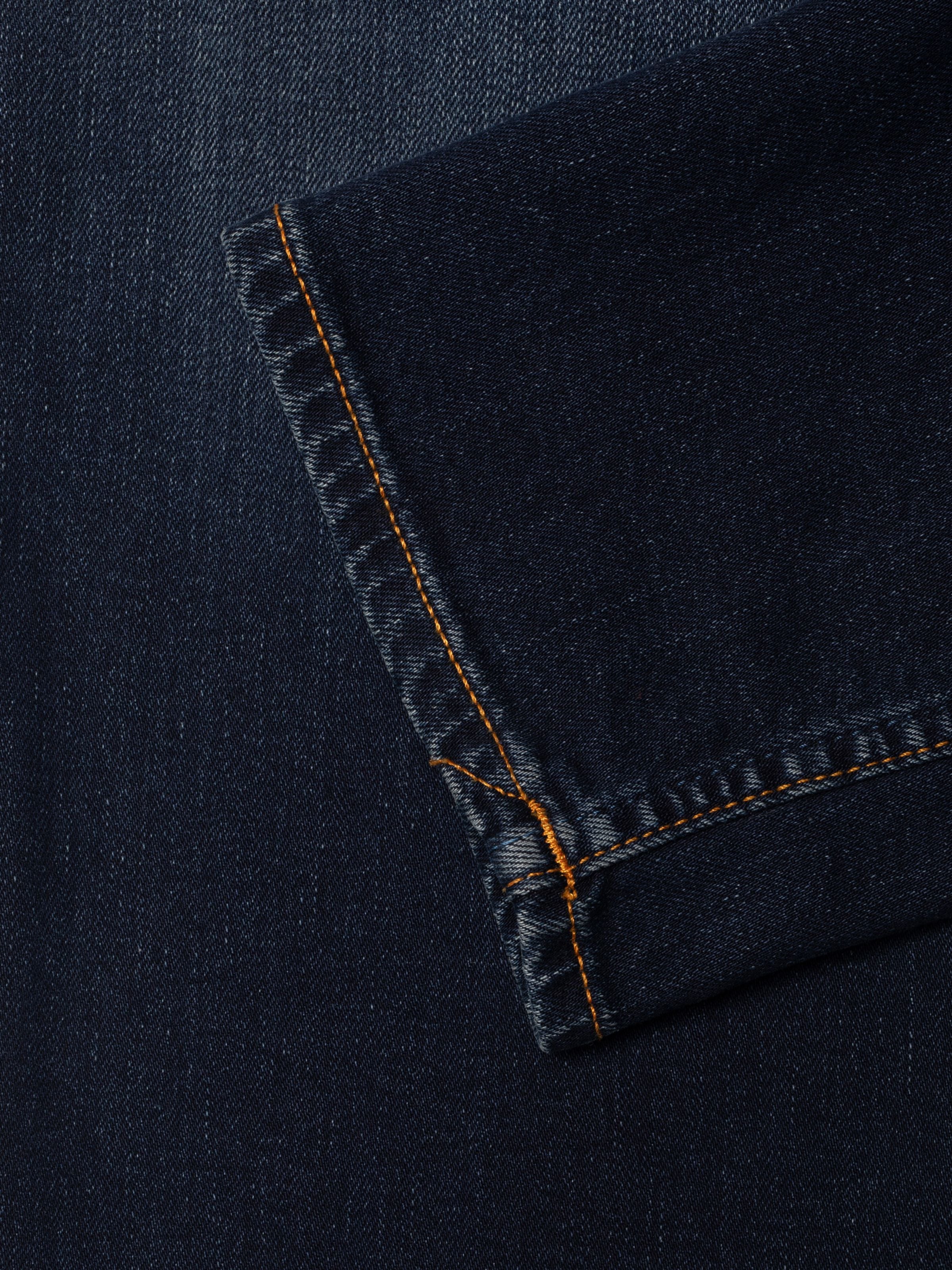 Nudie Jeans Solid Ollie Midnight Sky, schmale Passform Jeans, Nahaufnahme des Beinsaums und der dunklen Stretch-Denim-Textur.