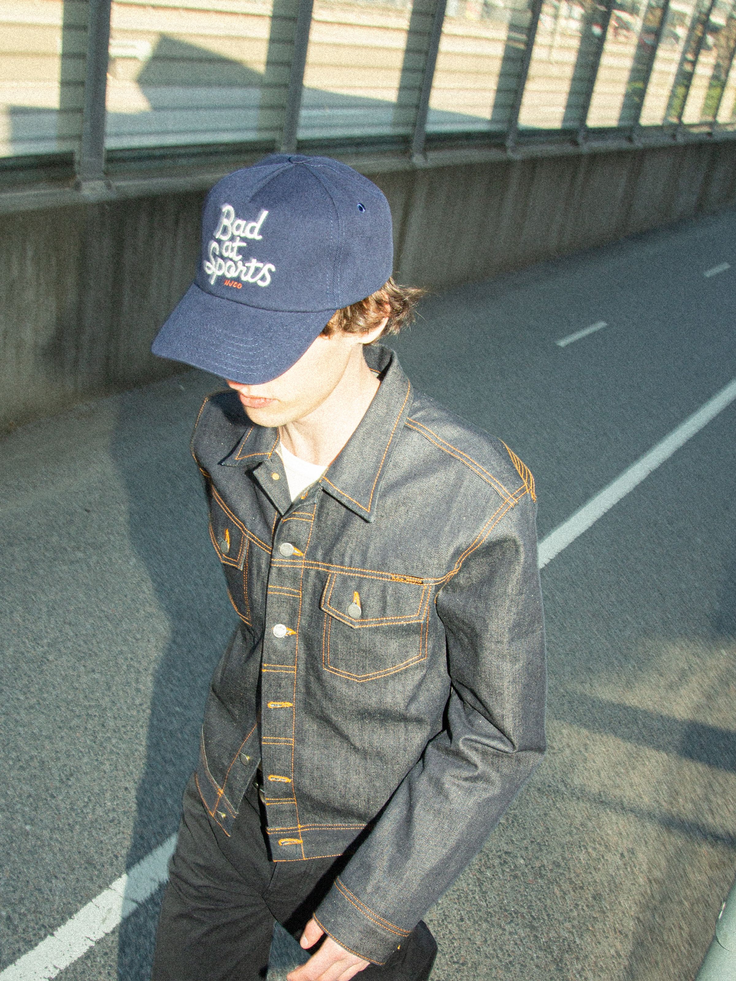 Nudie Jeans Nudie Cap Bad At Sports in dark blue organic cotton, featuring white embroidery, shown on a model.