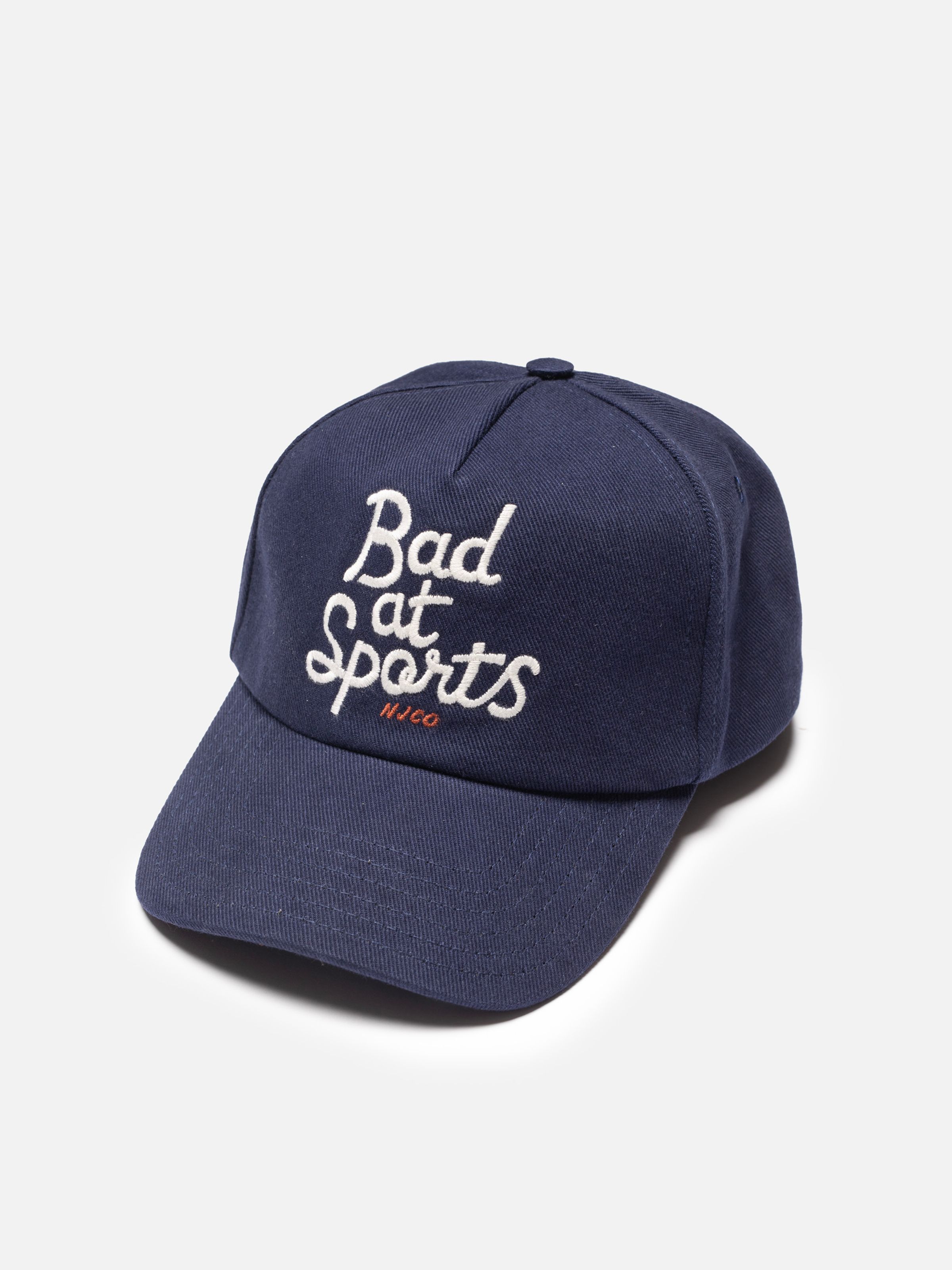 Nudie Cap Bad At Sports, a five-panel cap in dark blue organic cotton twill with white embroidery, shown flat.