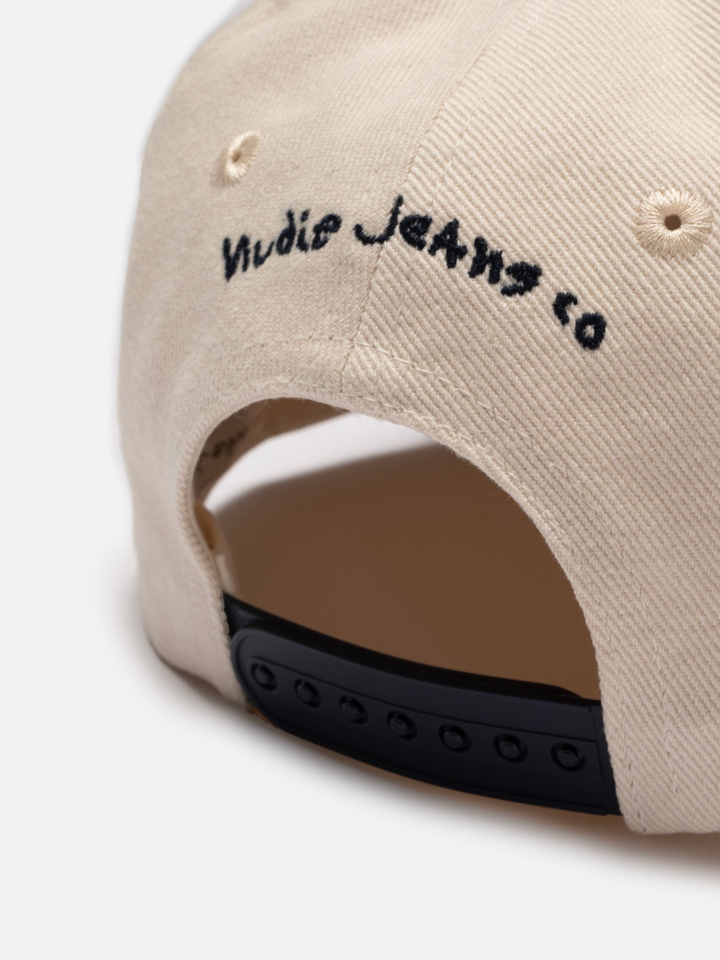 Nudie Cap Embo in Offwhite cotton, close-up of the back showing black logo embroidery and a snapback closure.