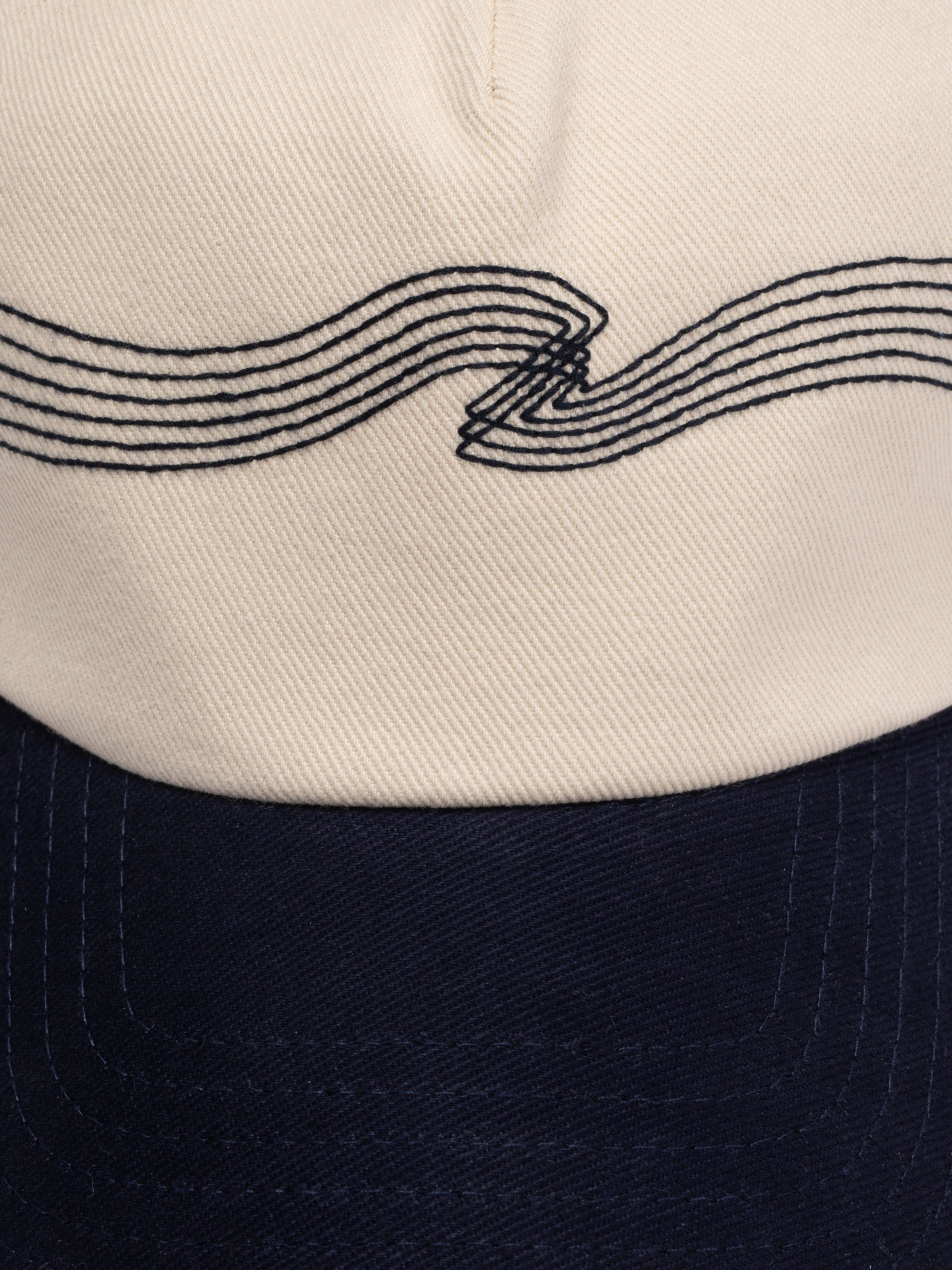 Nudie Cap Embo in off-white organic cotton twill, featuring navy wave embroidery and a contrasting navy brim.