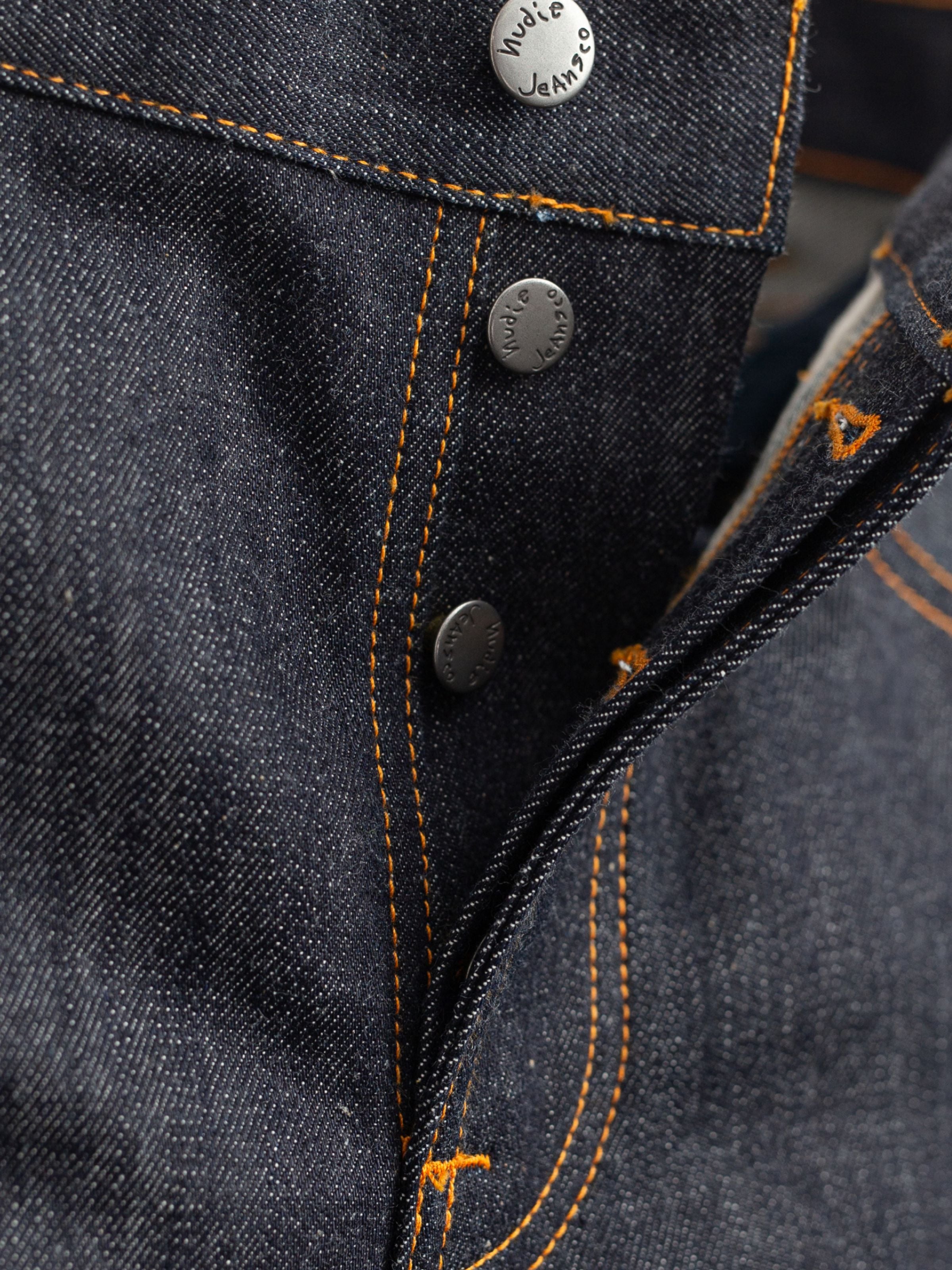Nudie Jeans Solid Ollie Dry Apex Selvage, close-up of the button fly and orange contrast stitching on raw selvedge denim.