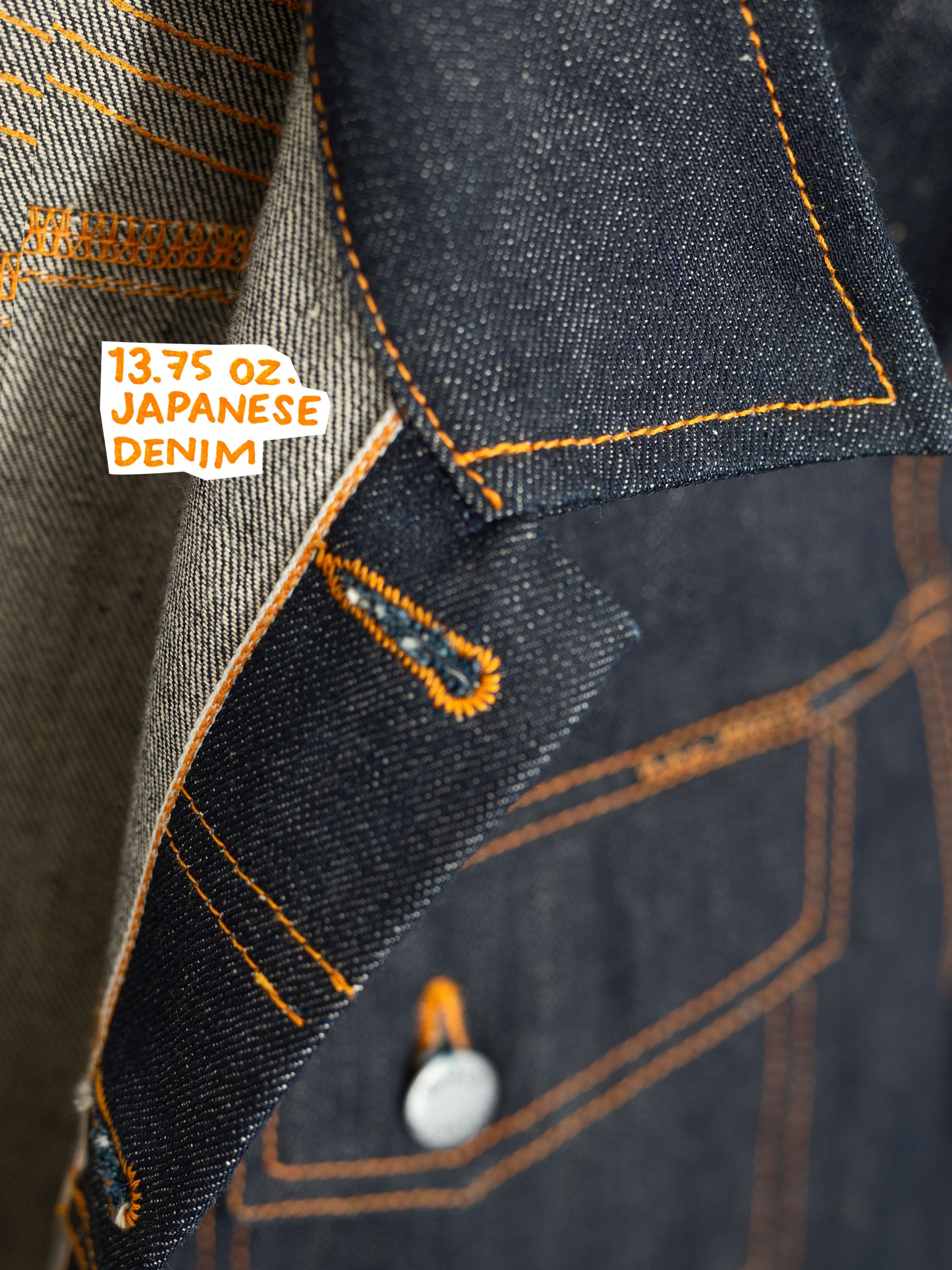 Nudie Jeans Conny Denim Jacket Dry Selvage, Nahaufnahme der starren Bio-Baumwoll-Selvedge-Denim-Textur und der orangen Nähte.