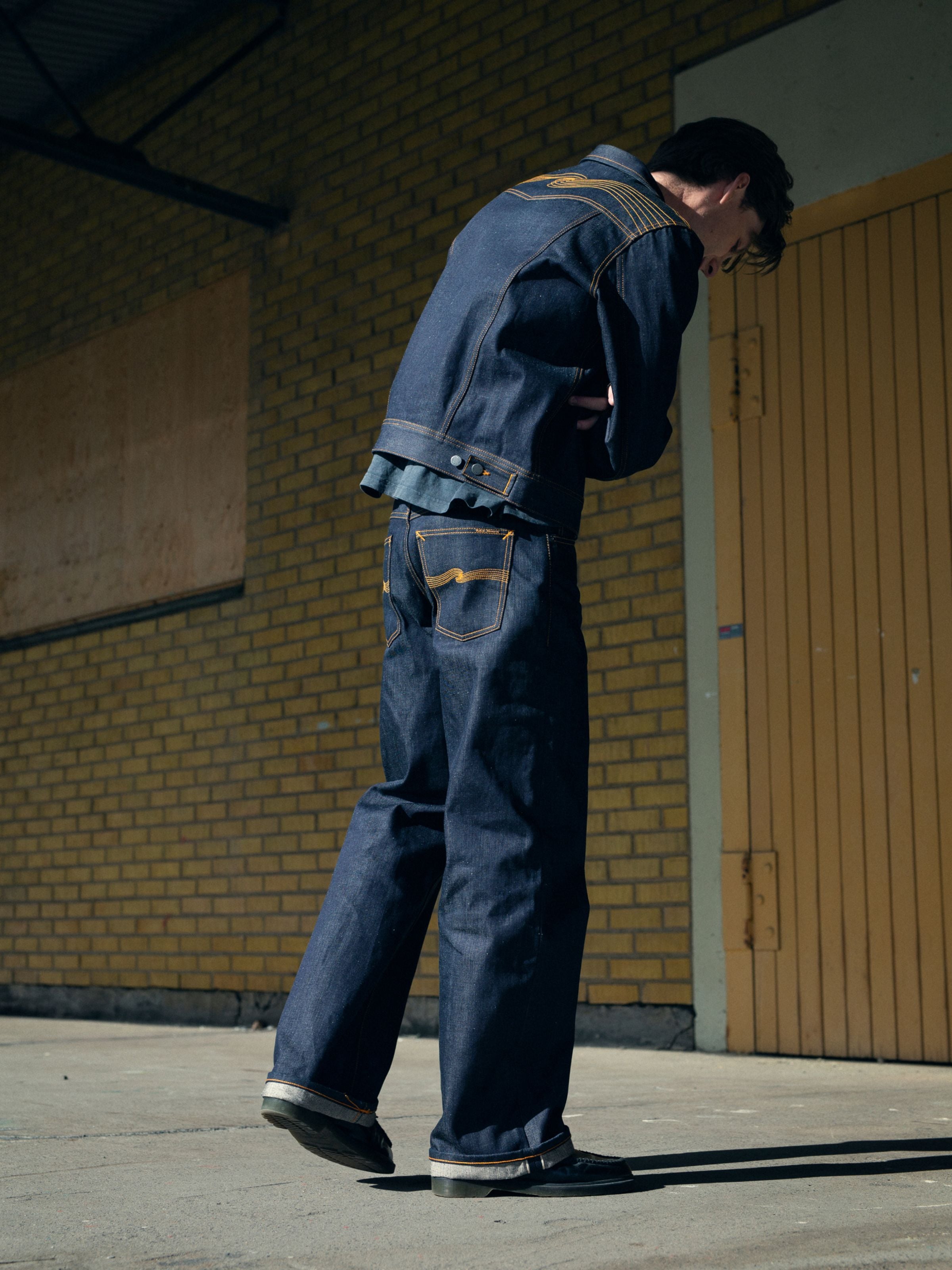 Nudie Jeans Conny Denim Jacket Dry Selvedge aus blauem Denim, an einem Model im Freien mit Rückenansicht gezeigt.