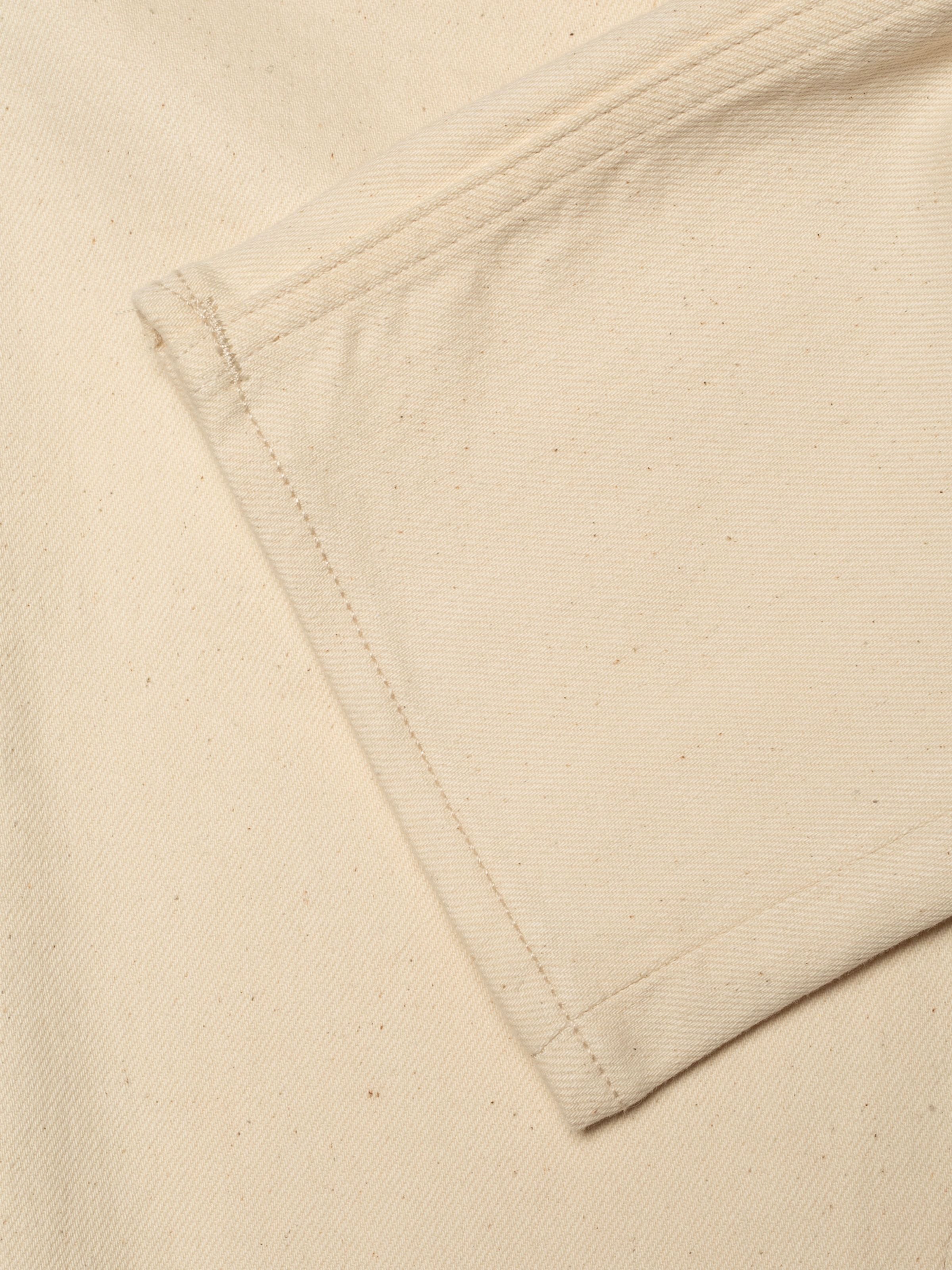 Nudie Jeans Lean Dean Ivory, close-up of ecru organic cotton stretch denim with irregular yarns and tonal stitching.