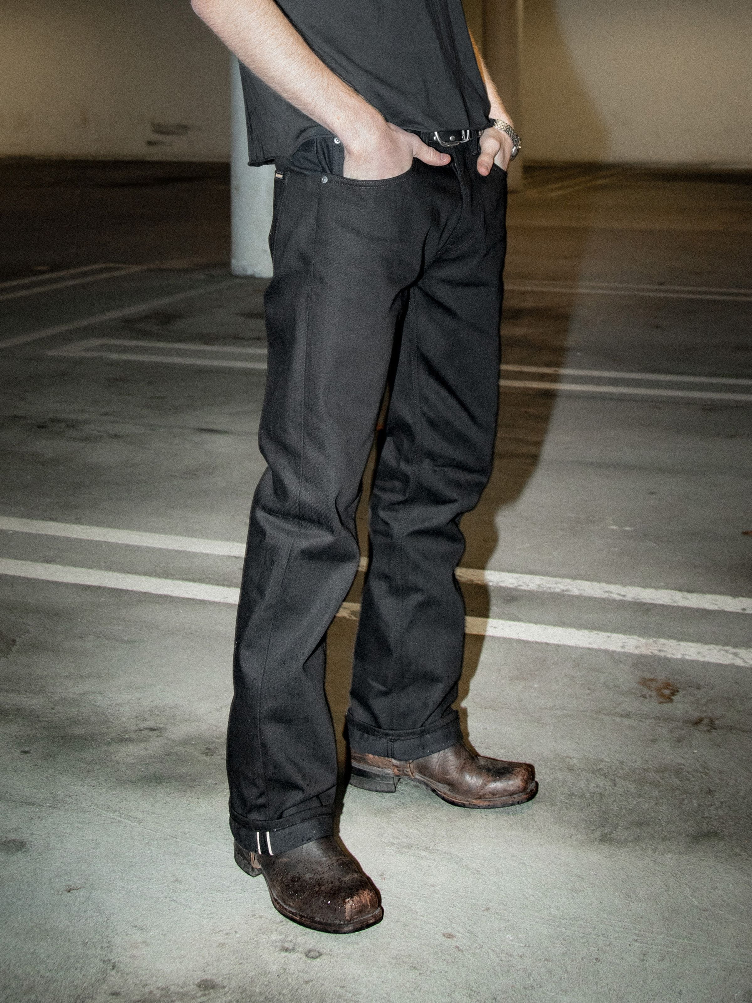 Nudie Jeans Regular Alf Dry Black Selvage, men's regular-fit selvedge jeans in black, shown worn outdoors with boots.